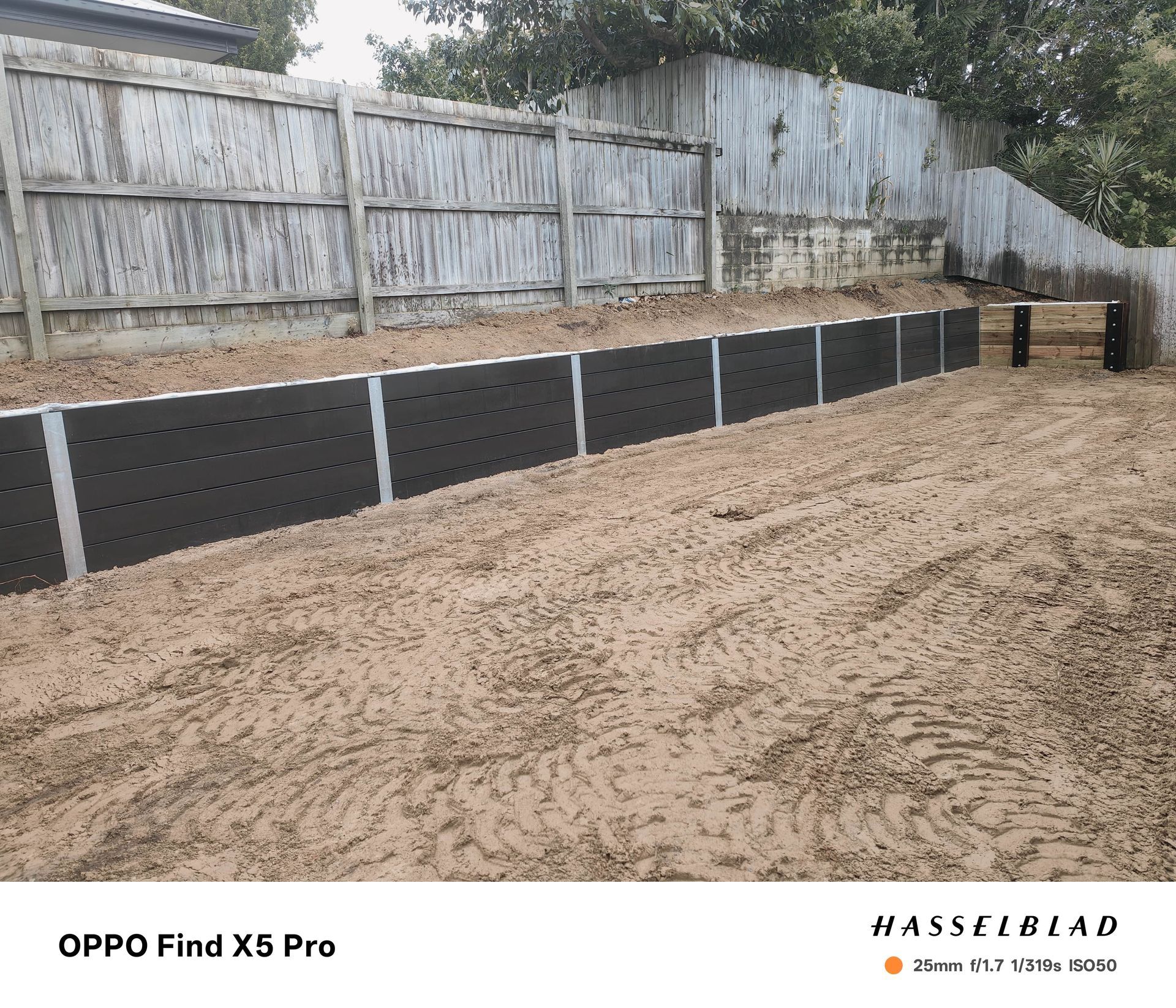 Black retaining wall with a wooden fence background on a dirt ground — Quality Fences 4 U in Gympie, QLD