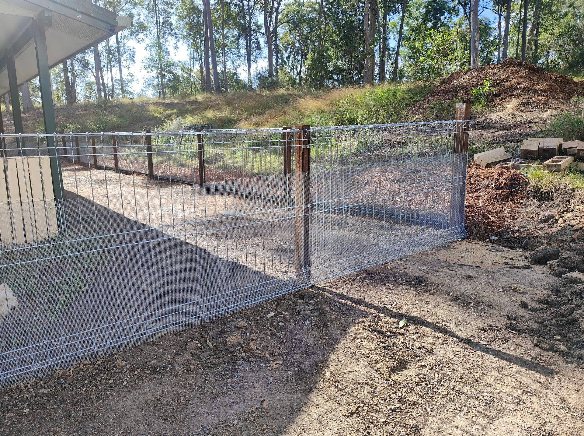 Chain-link Fencing Around A Dirt Path Beside A House, With Trees And A Grassy Slope In The Background — Quality Fences 4 U in Gympie, QLD
