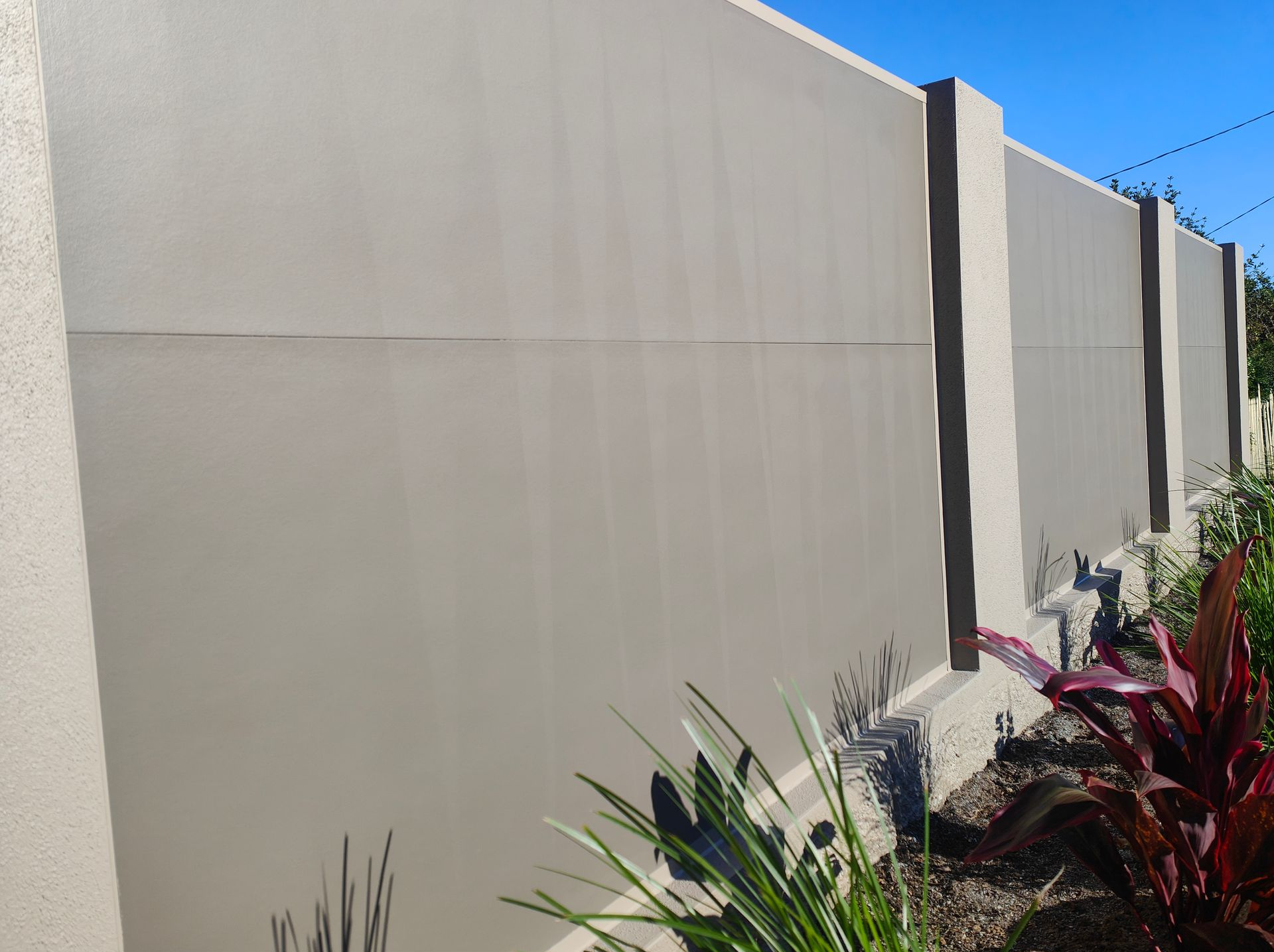 Beige Stucco Wall With Dark Posts Beside A Landscaped Garden And Blue Sky — Quality Fences 4 U in Gympie, QLD