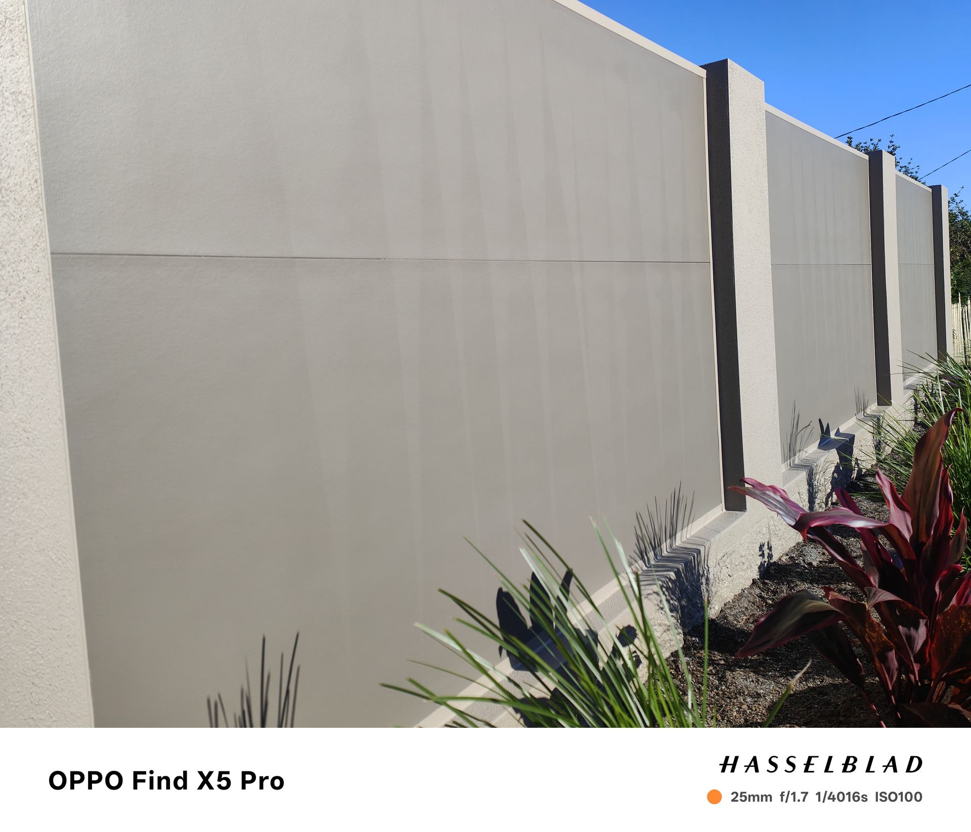 Gray concrete wall with brown pillars, plants in foreground, bright sky — Quality Fences 4 U in Gympie, QLD
