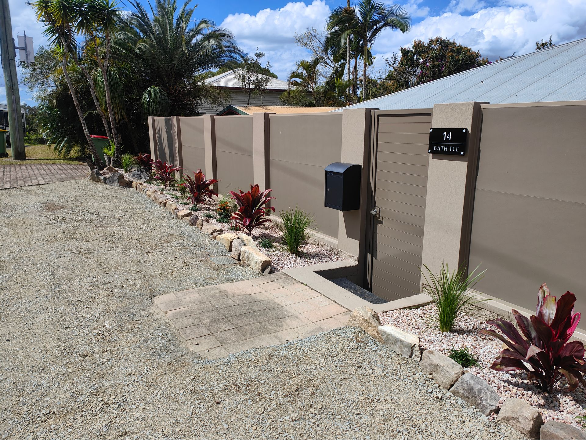 Residential Driveway With Beige Wall, Black Mailbox, Gravel, And Red Landscaping Plants Under A Sunny Sky — Quality Fences 4 U in Gympie, QLD