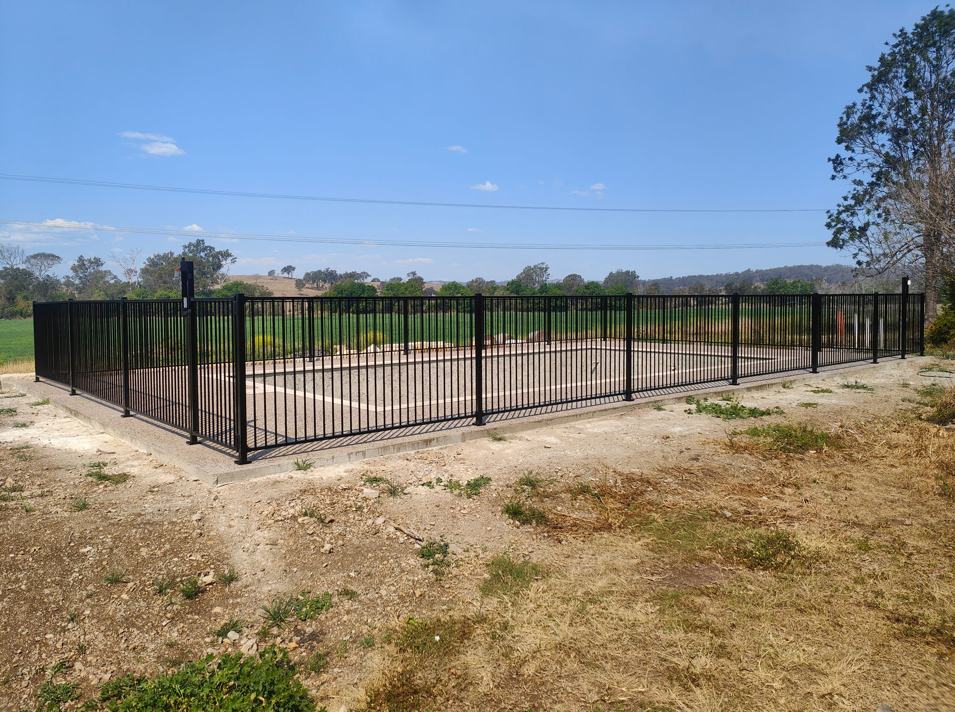 Black Metal Fence Enclosing A Bare Dirt Field Under A Clear Blue Sky — Quality Fences 4 U in Gympie, QLD