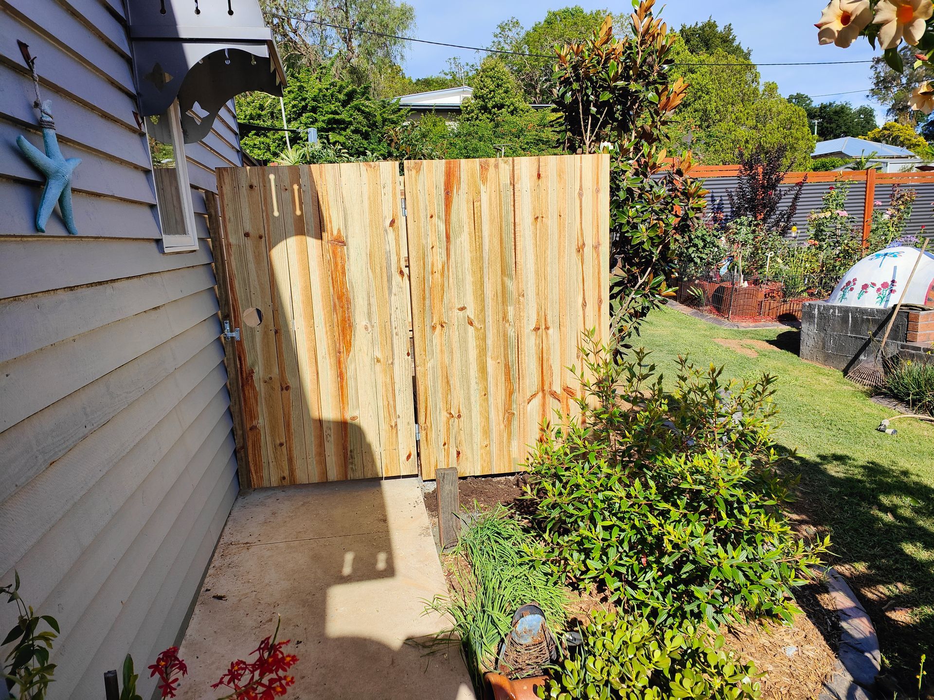 Wooden Gate And Fence Beside A House, With A Narrow Concrete Path And Garden Plants In Bright Sunlight — Quality Fences 4 U in Gympie, QLD