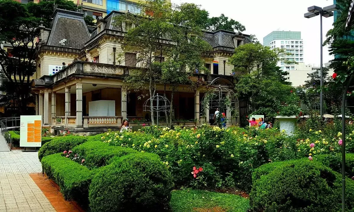 Uma casa grande é cercada por arbustos e árvores em um parque.