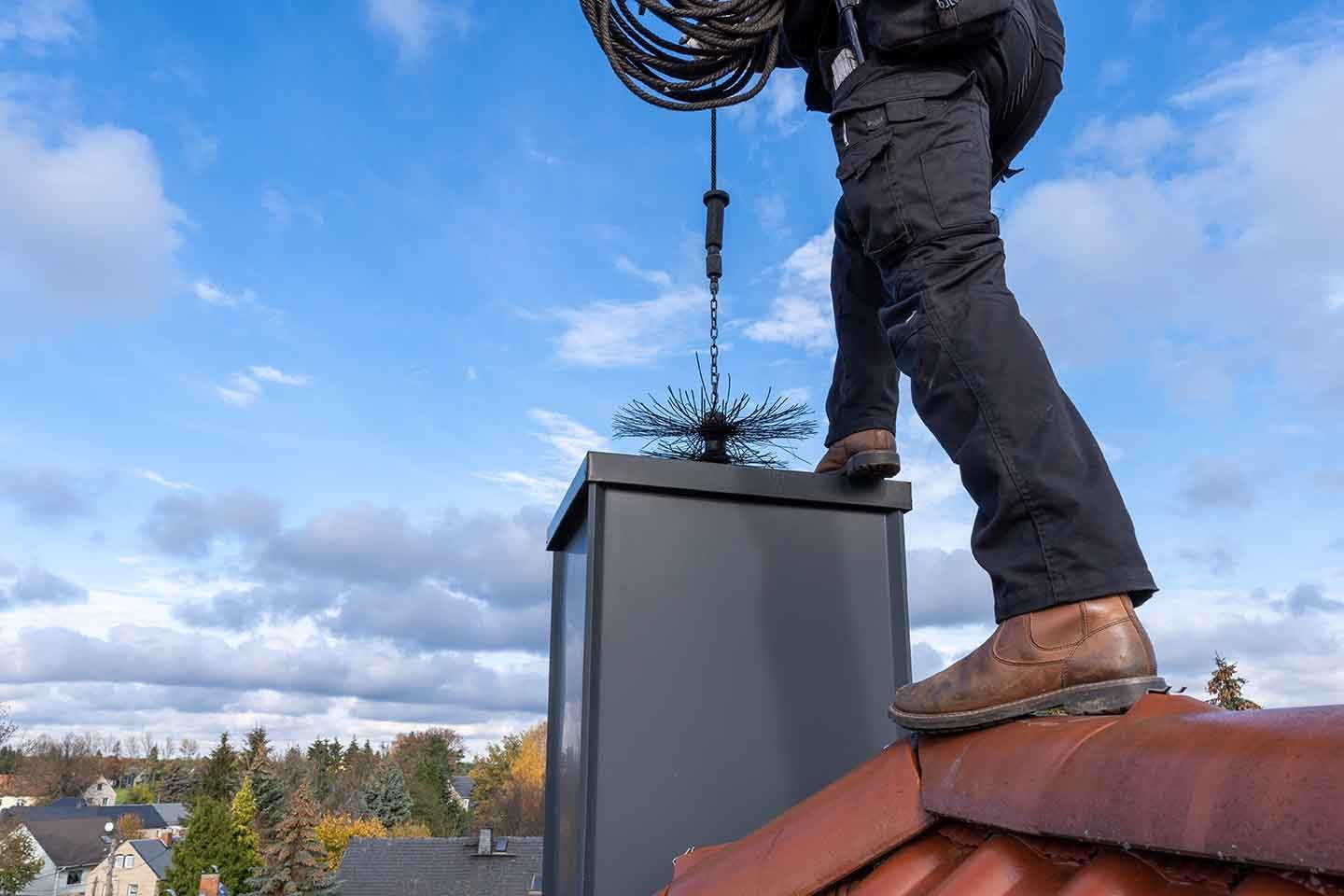 Chimney sweep cleaning a chimney standing on the house roof – Macungie, PA - Anytime Todd's Chimney Sweeping