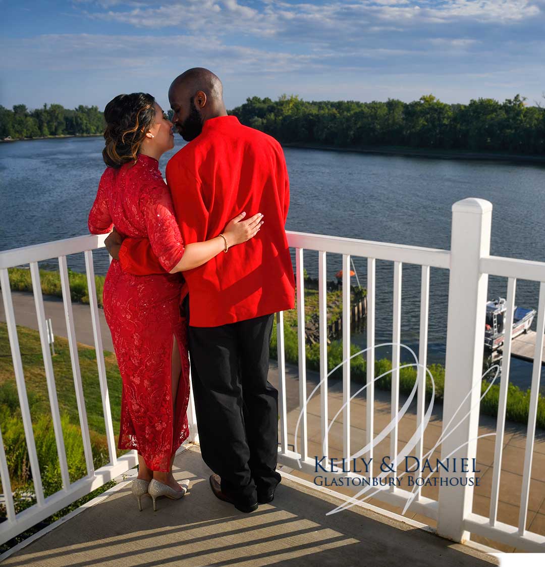 Wedding Couple in red clothing embracing on a balcony overlooking a river at sunset