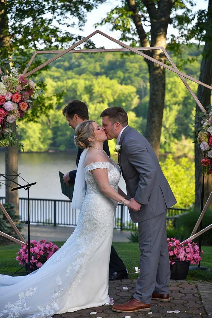 Bride and groom kissing under a floral arch at an outdoor wedding ceremony