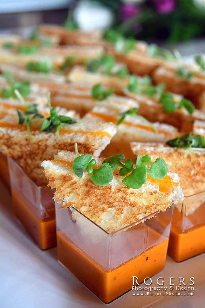 Rows of clear cups filled with orange soup, topped with frothy cream and green herbs.