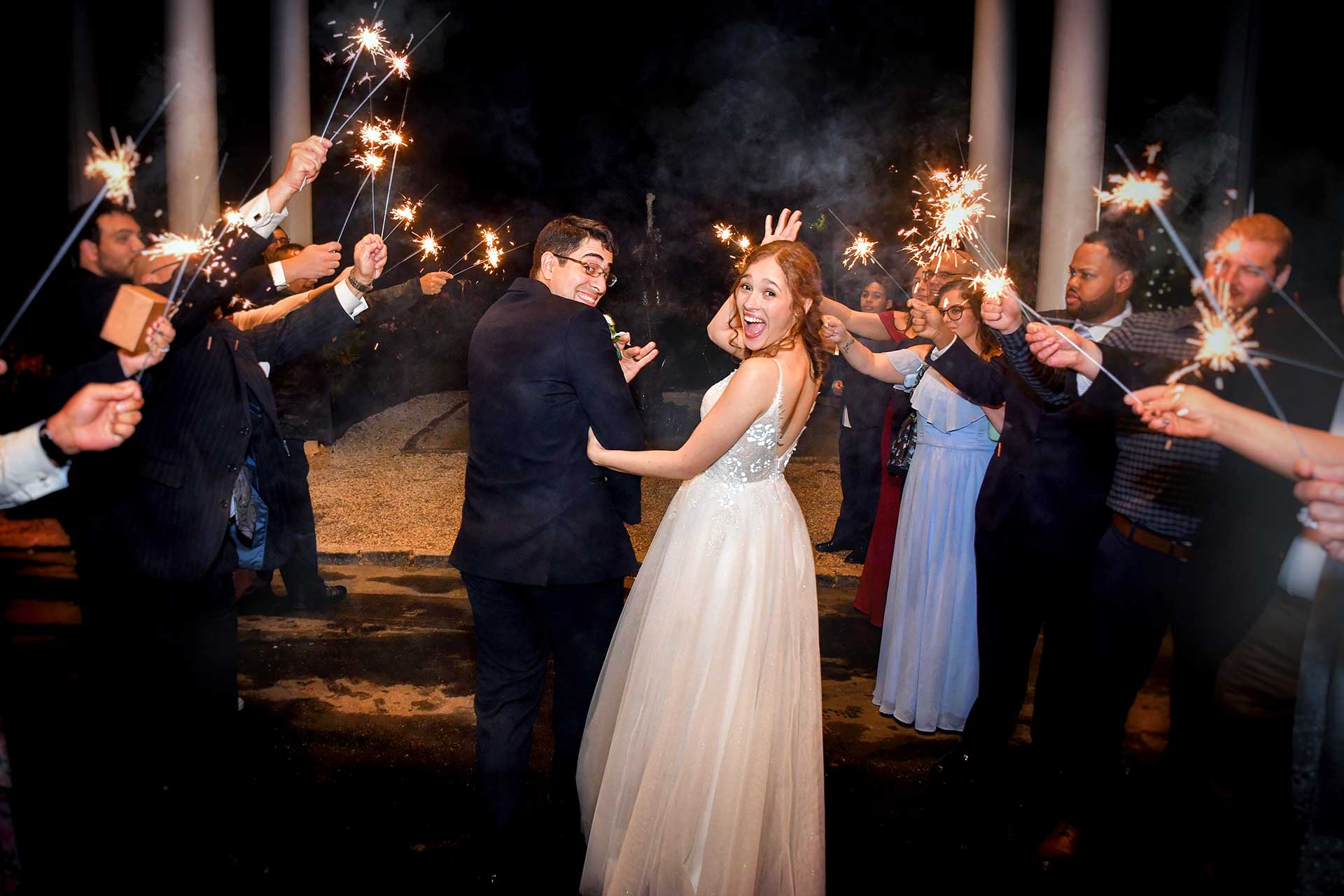 A bride and groom are surrounded by their wedding guests holding sparklers at Woodwinds wedding photographed by Rogers Photography in Connecticut. 