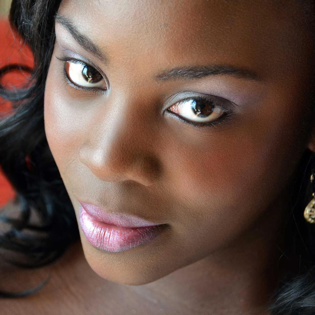 Close-up portrait of a woman with glossy pink lips and dark hair against a warm orange background