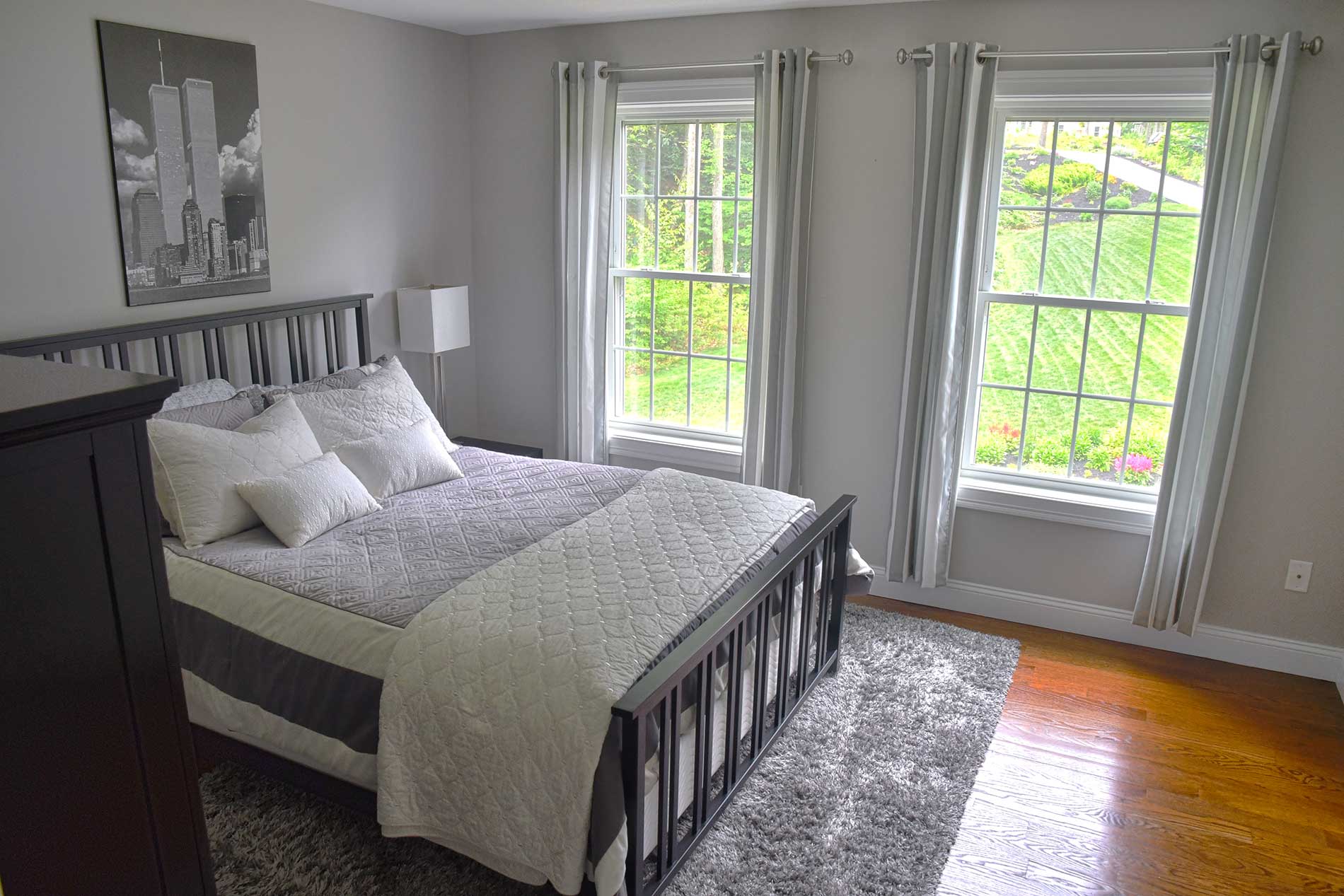 Bright bedroom with a bed, gray rug, and two large windows letting in sunlight