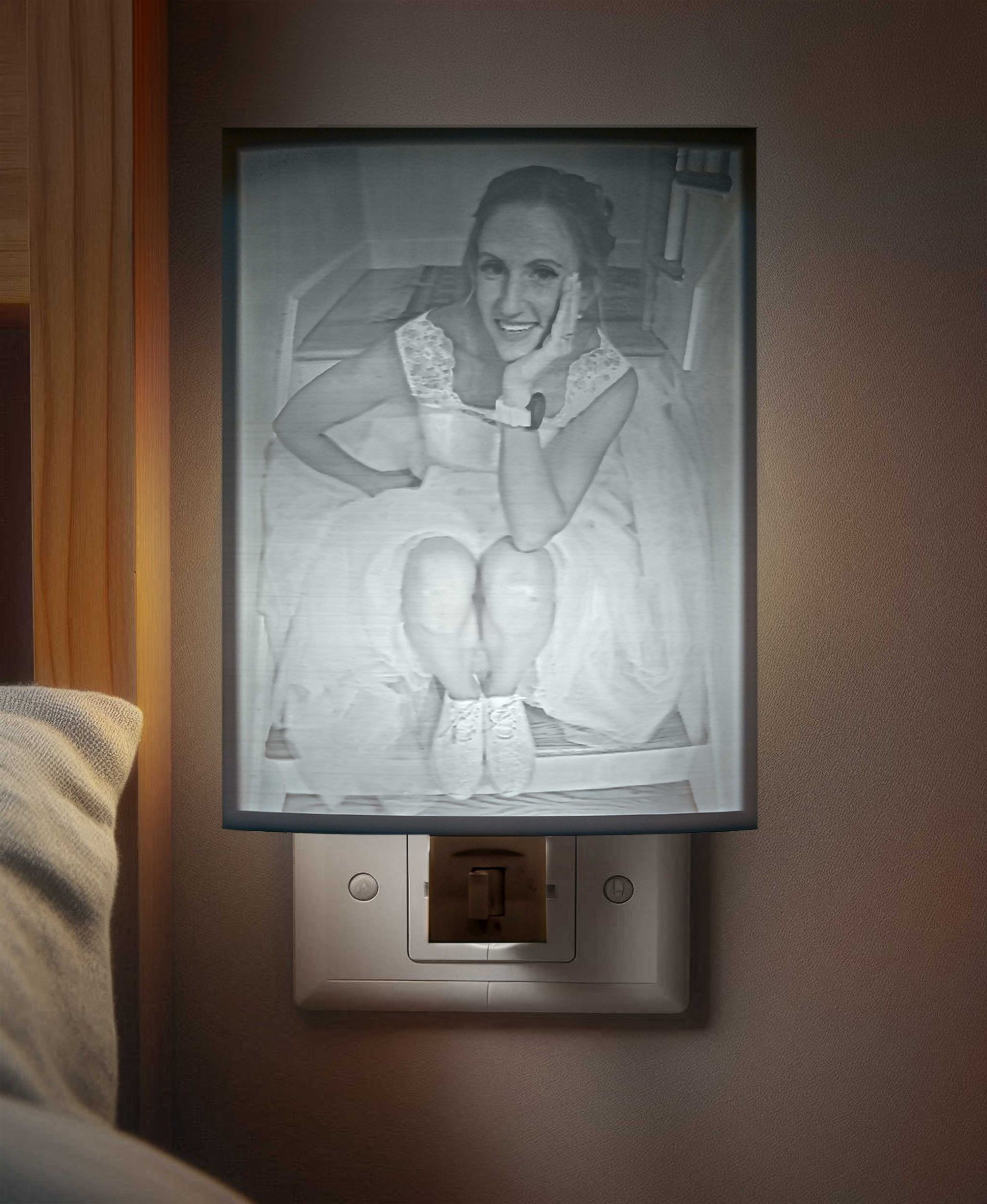 Framed black-and-white portrait above a wall light switch, showing a smiling person seated with knees up.