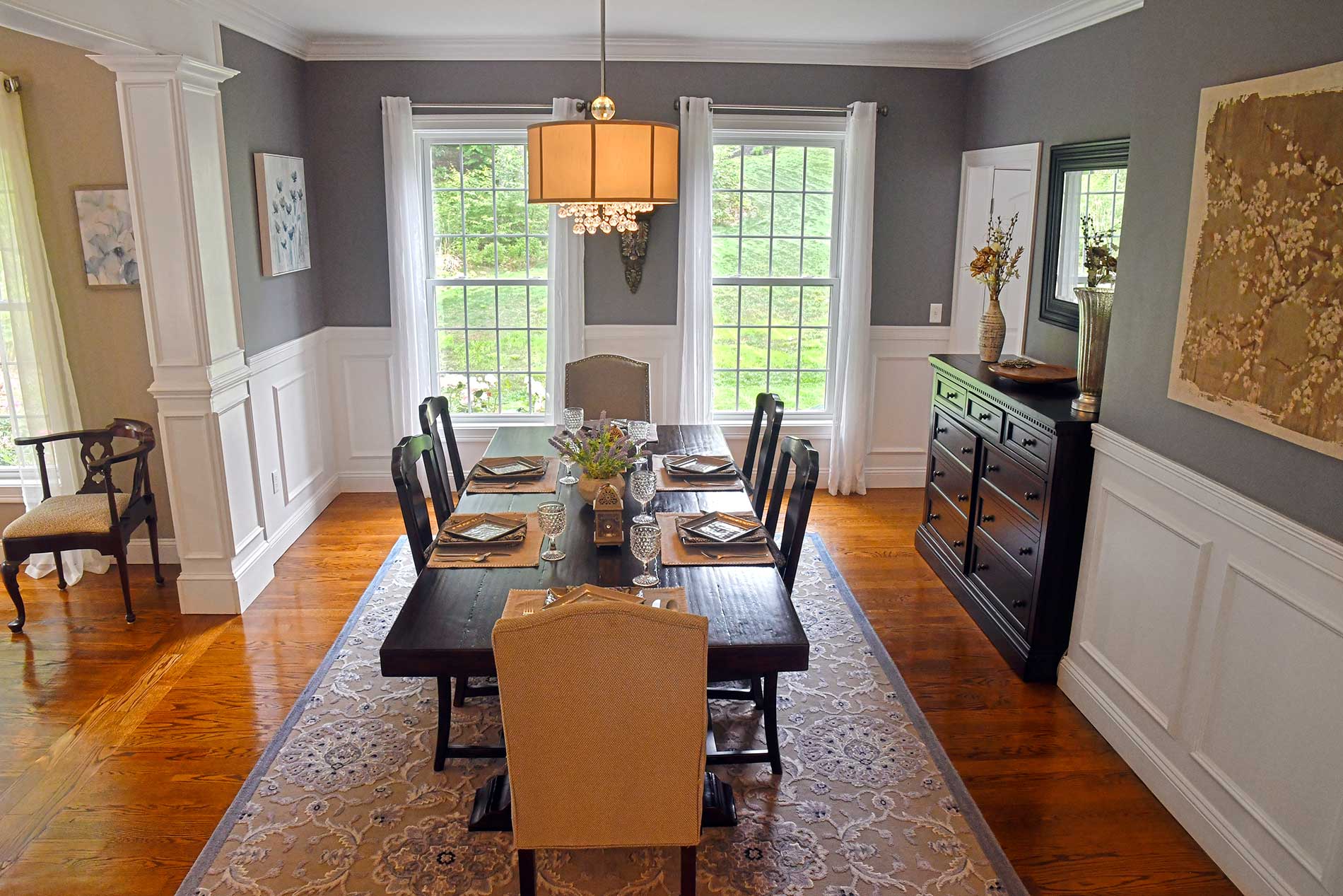 Elegant dining room with hardwood floors, patterned rug, dark table, and large windows with white curtains