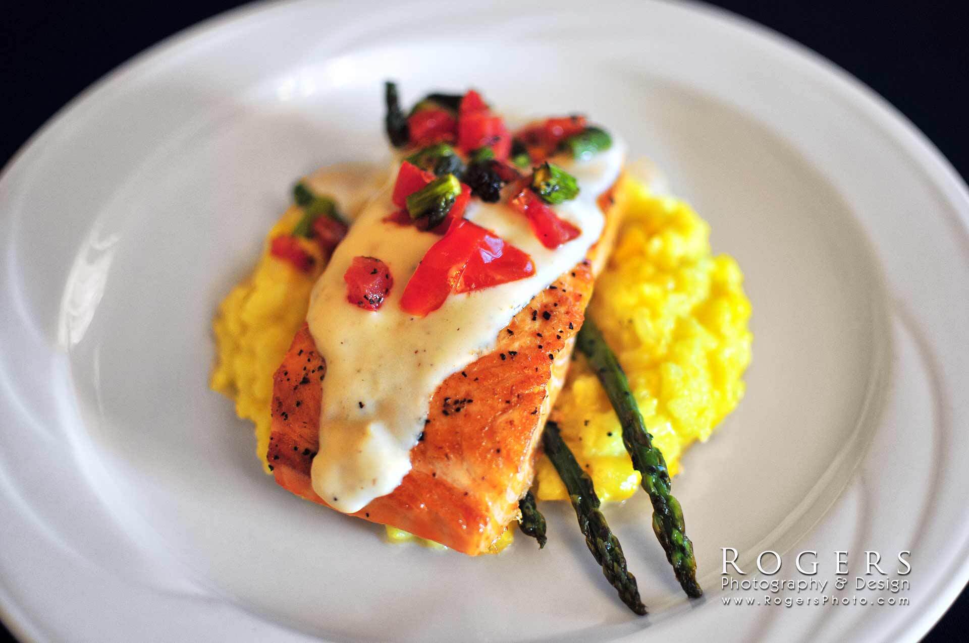 Seared salmon with herb sauce, pomegranate garnish, asparagus, and yellow risotto on a white plate
