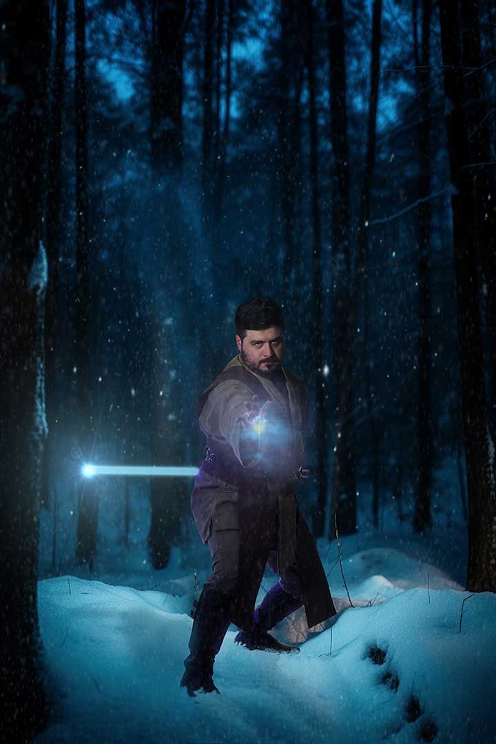 Person holding a glowing blue sword in a snowy, dark forest at night