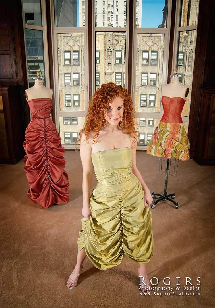 Fashion designer Holly Kristen in a yellow ruched dress standing in a boutique with mannequins and large windows behind her.
