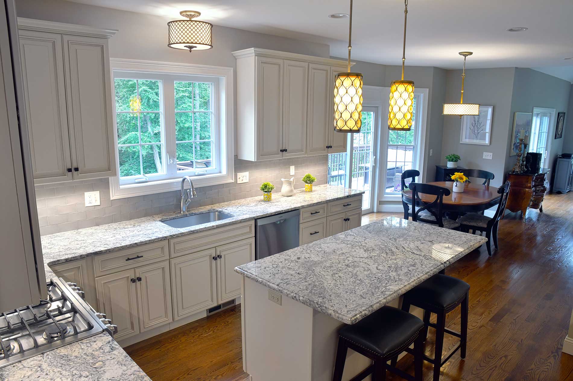 Bright kitchen with white cabinets, large window, island, and wood floors open to a dining area.