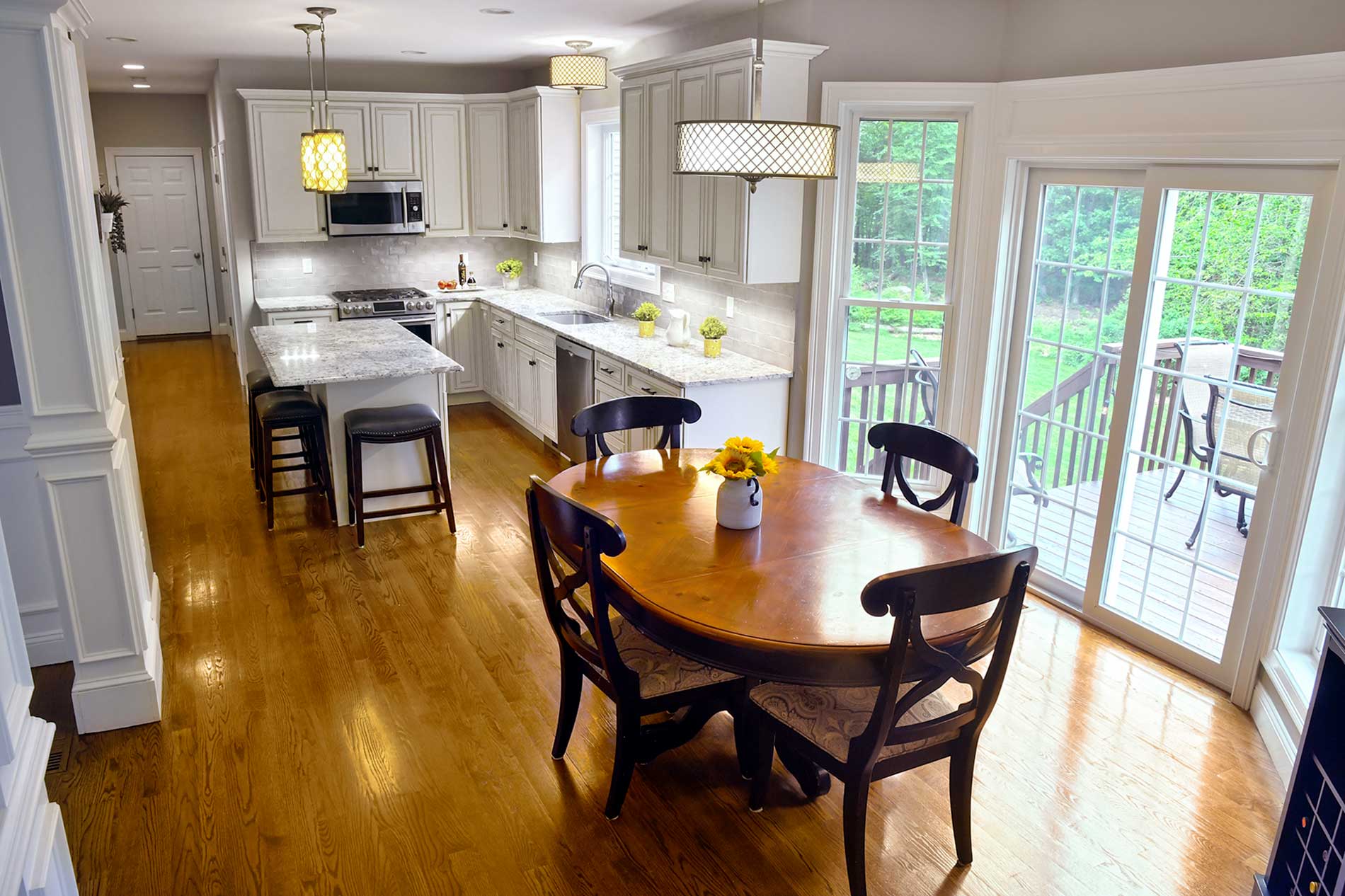 Bright kitchen and dining area with wooden floors, white cabinets, round table, and sliding glass doors to a deck