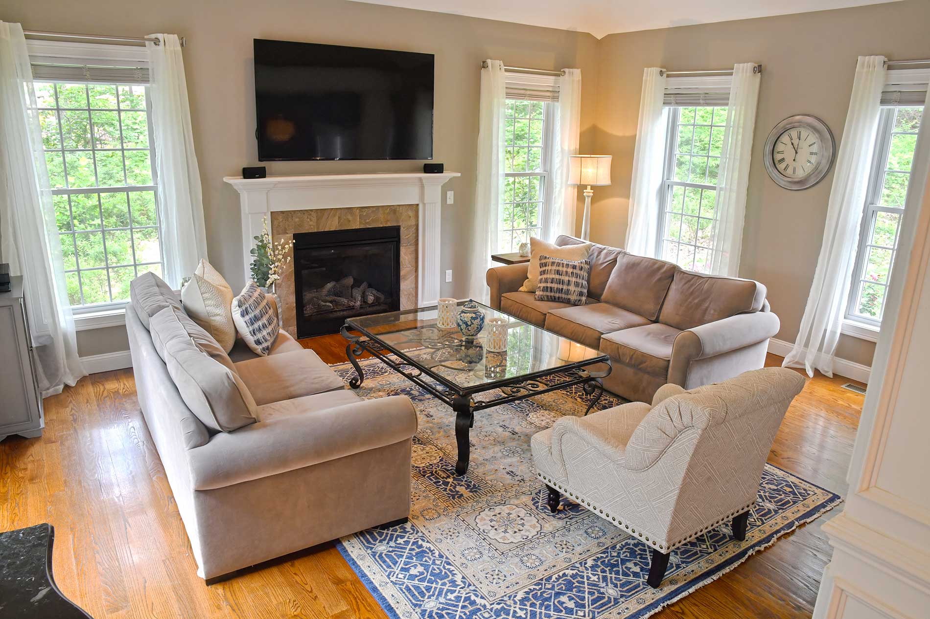 Bright living room with fireplace, sofas, glass coffee table, blue rug, and large windows
