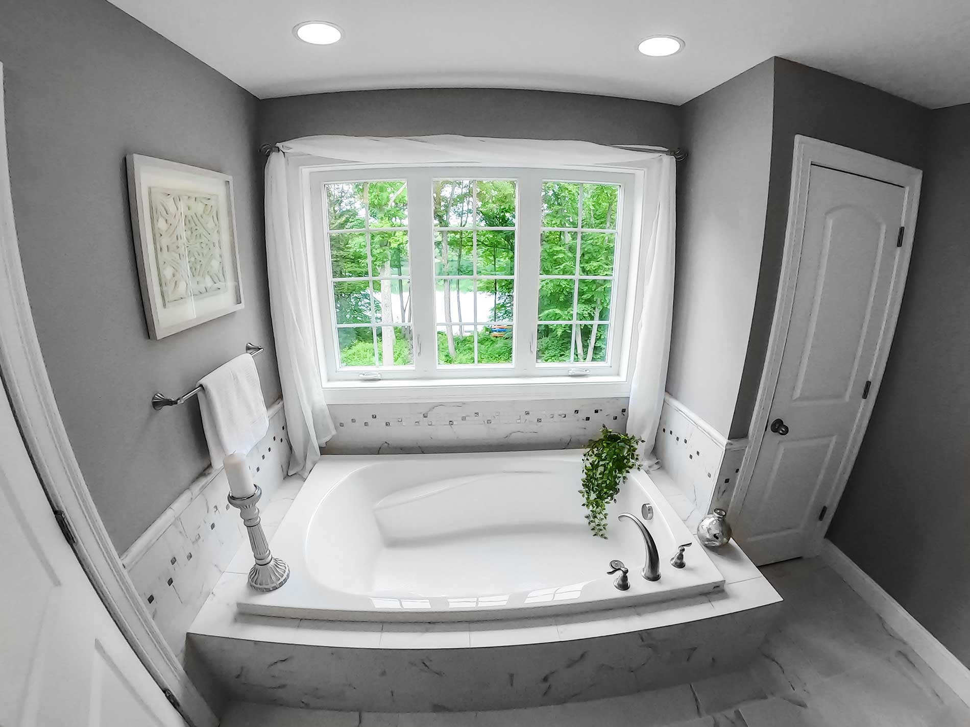 Modern gray bathroom with a white soaking tub, window, and potted plant