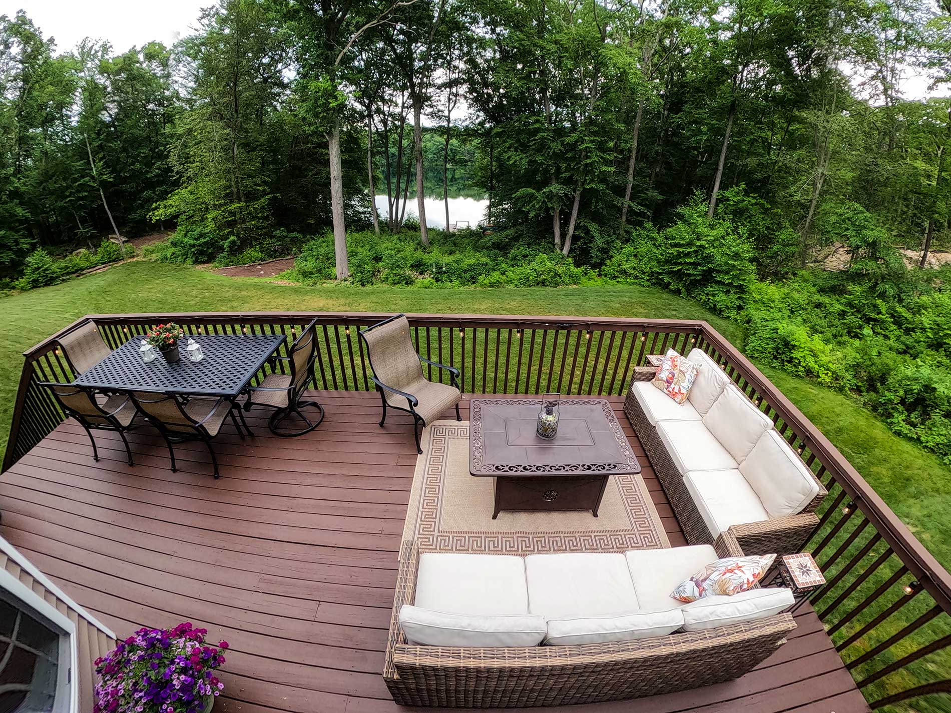 Deck with white patio furniture, table, and grill overlooking a green backyard garden