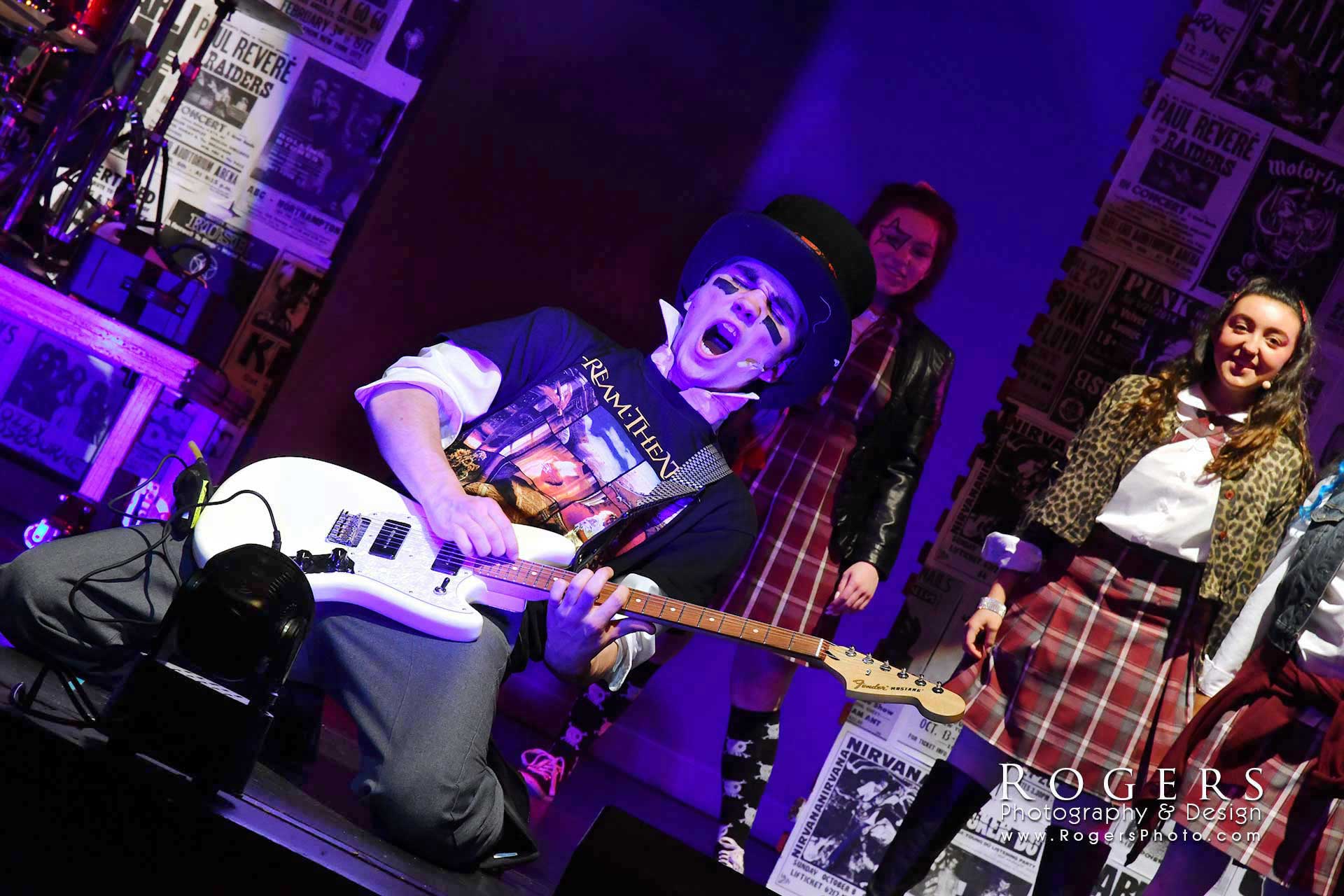 Three musicians performing on a neon-lit stage, one playing guitar in the foreground.