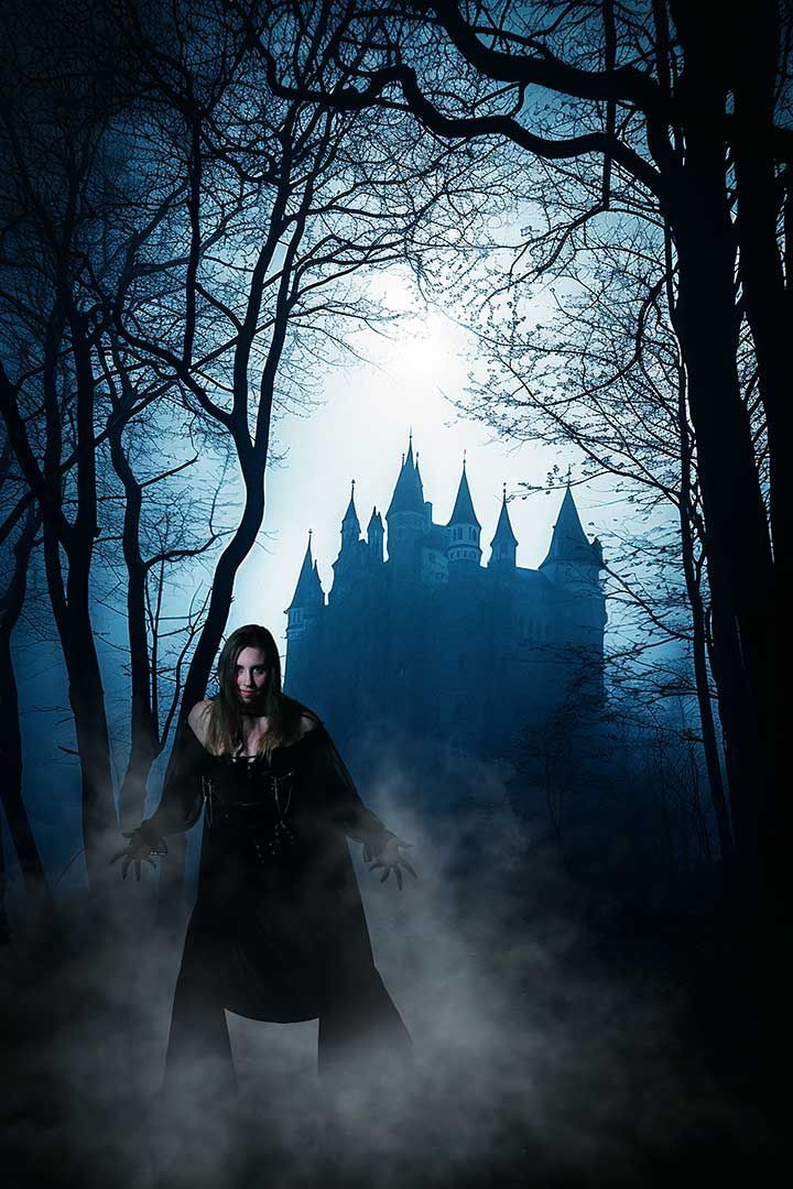 Cosplay Witch Dark cloaked figure stands in fog before a blue-lit castle in a haunted forest
