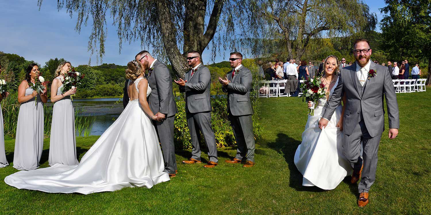 Wedding party posing outdoors on a sunny lawn, with bride in a white gown and guests in gray suits.