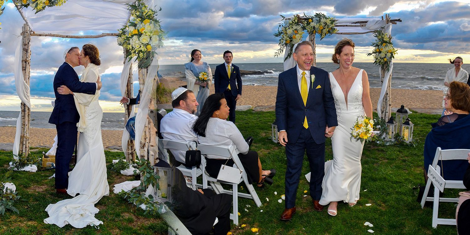 Outdoor wedding ceremony by the water, with bride and groom standing under a floral arch.