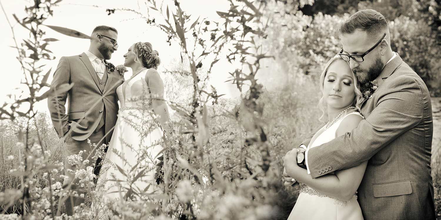 Two couples standing in a flower garden, one embracing in the foreground and one in the background.