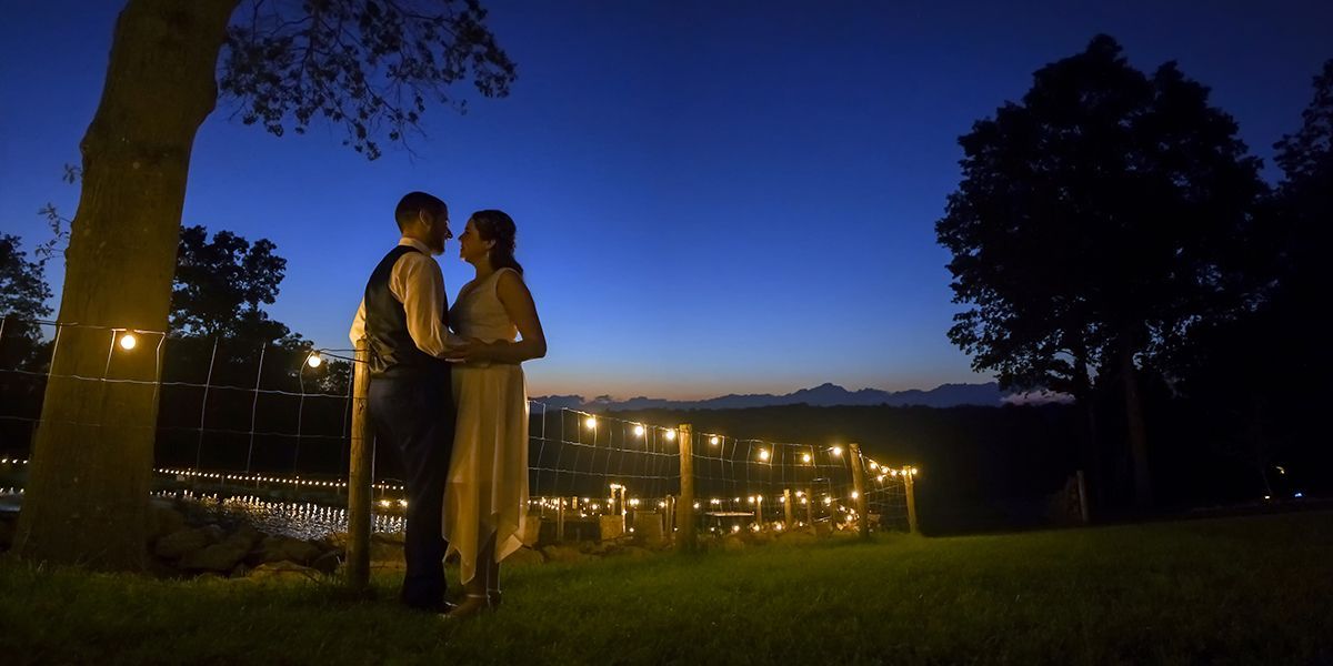 Couple standing together at dusk in a park, with city lights and a deep blue sky in the background