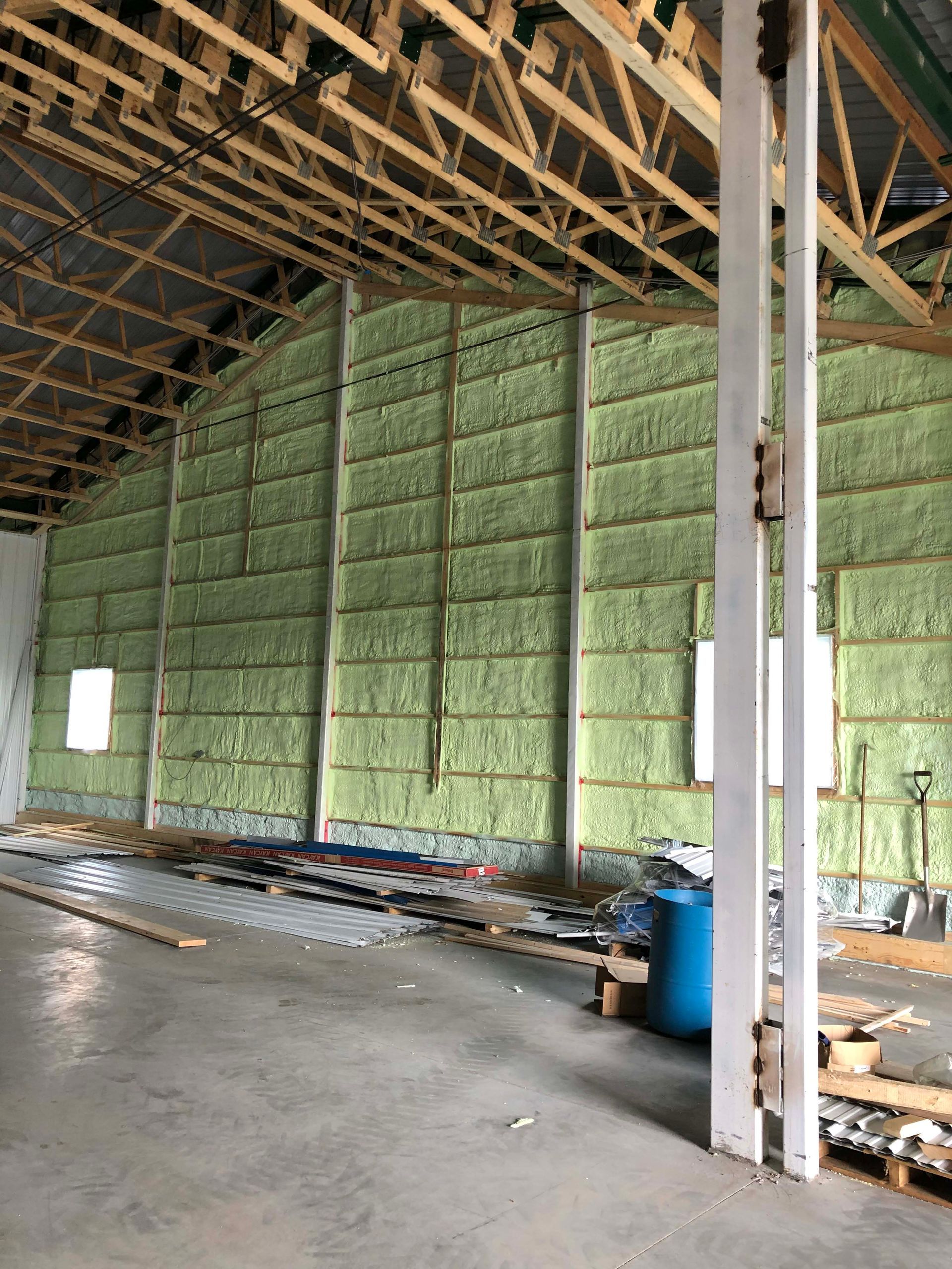 Interior of an unfinished building with exposed roof trusses and green insulated walls.