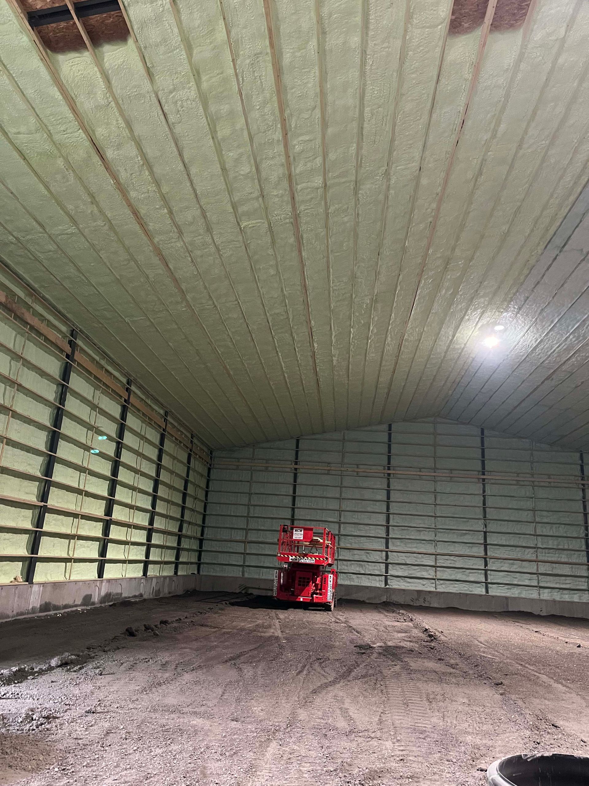 Empty warehouse with a red industrial lift on a dirt floor under a high curved ceiling