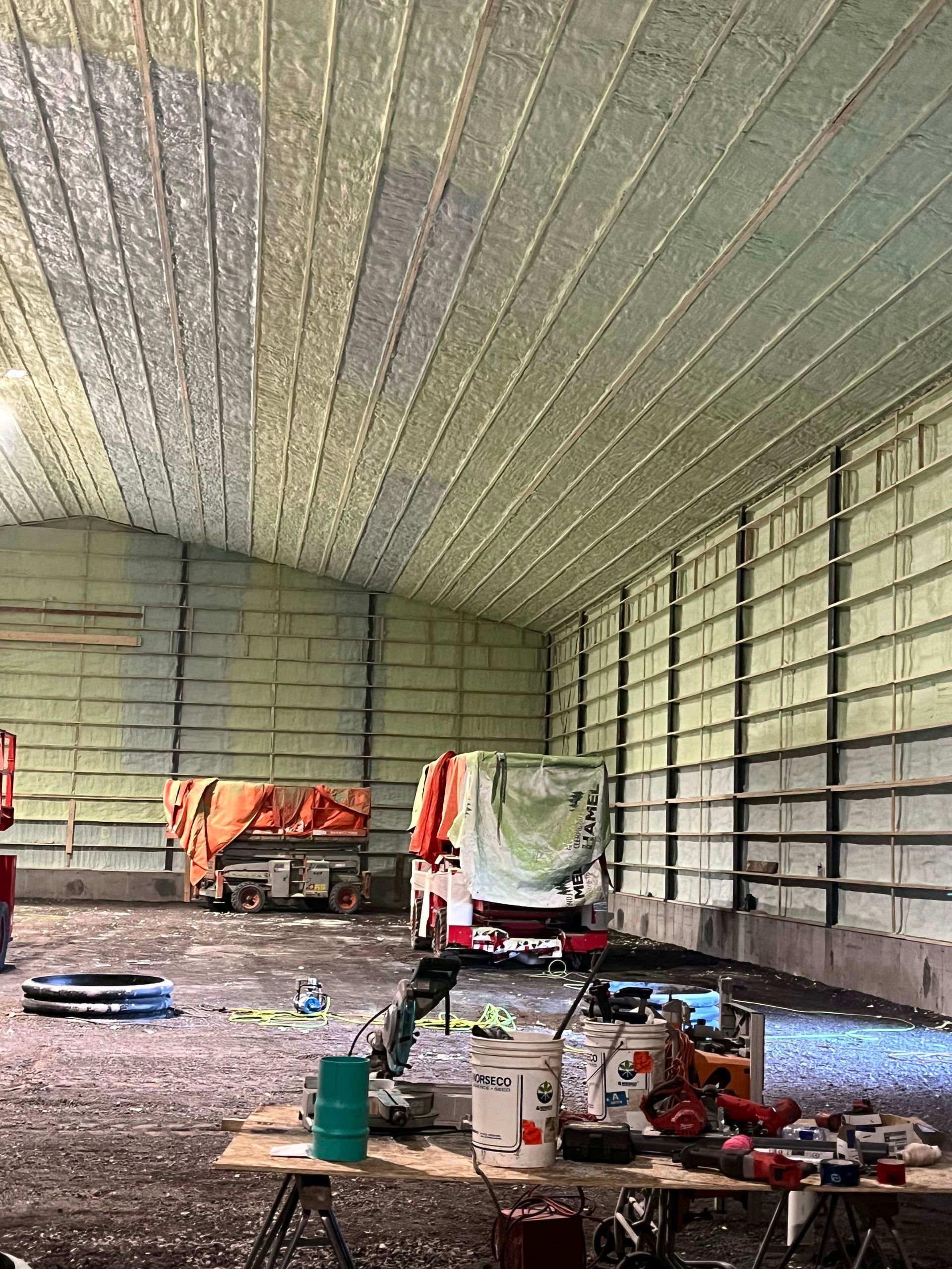 Inside of a large insulated metal building under construction, with tools and equipment scattered on the floor.