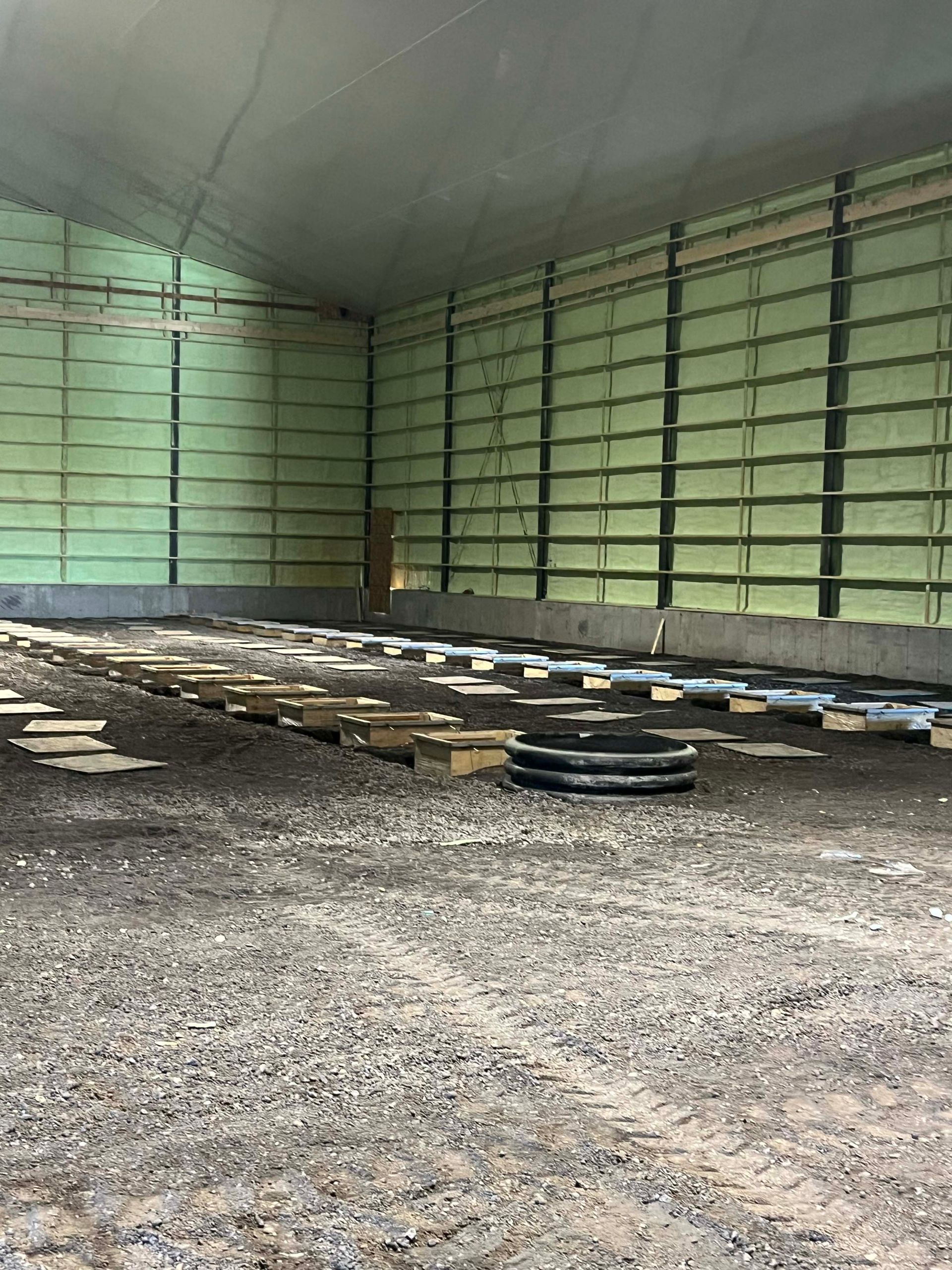 Empty indoor greenhouse with green walls, gravel floor, and stacked materials on the ground
