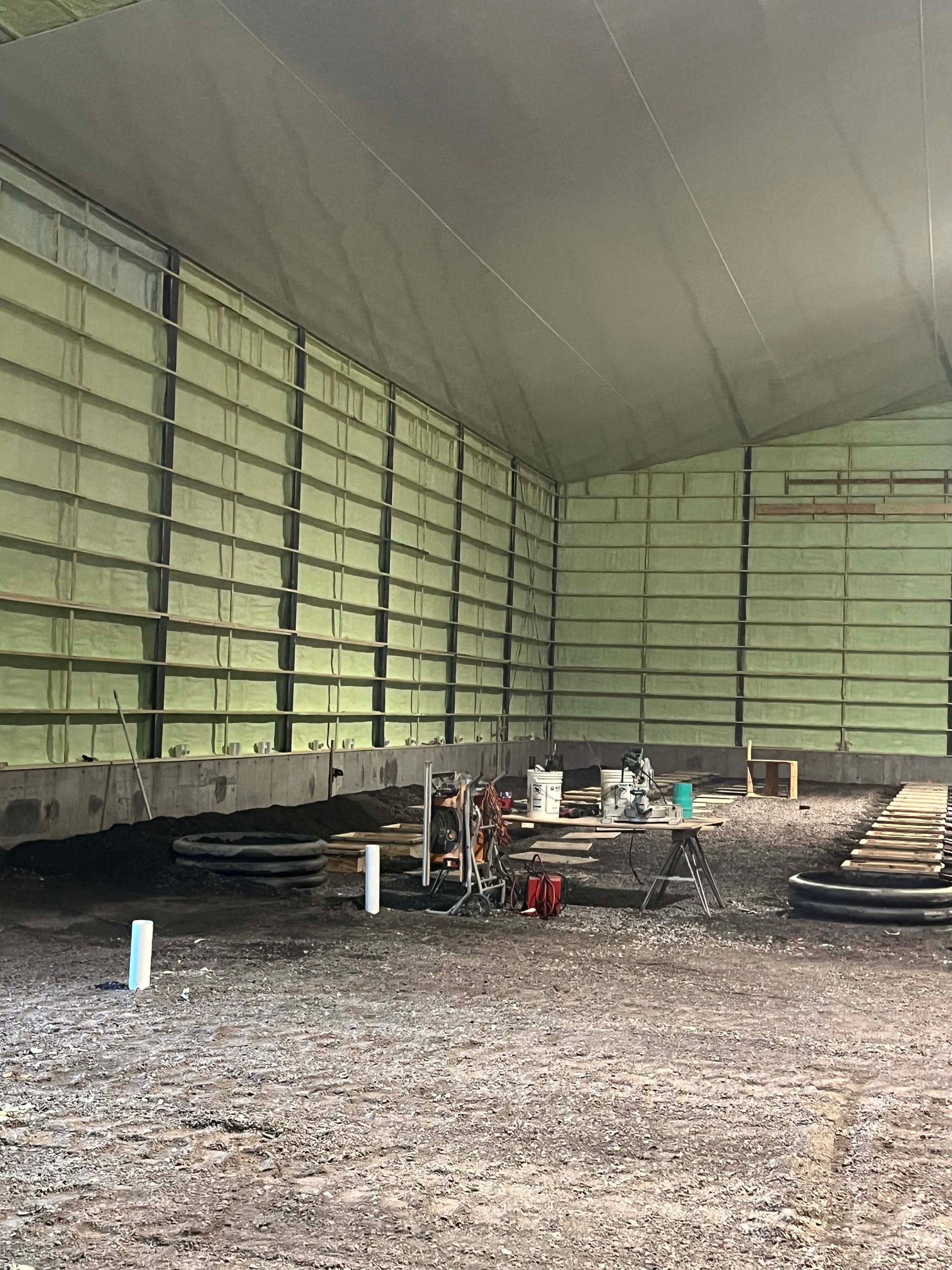 Empty large tent interior with metal walls, gravel floor, and scattered equipment near the back.
