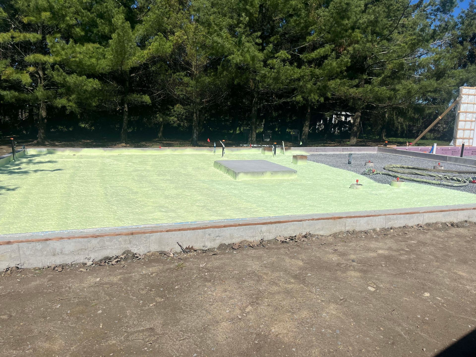 Covered foundation slab in a wooded area, with concrete edges and a dirt foreground