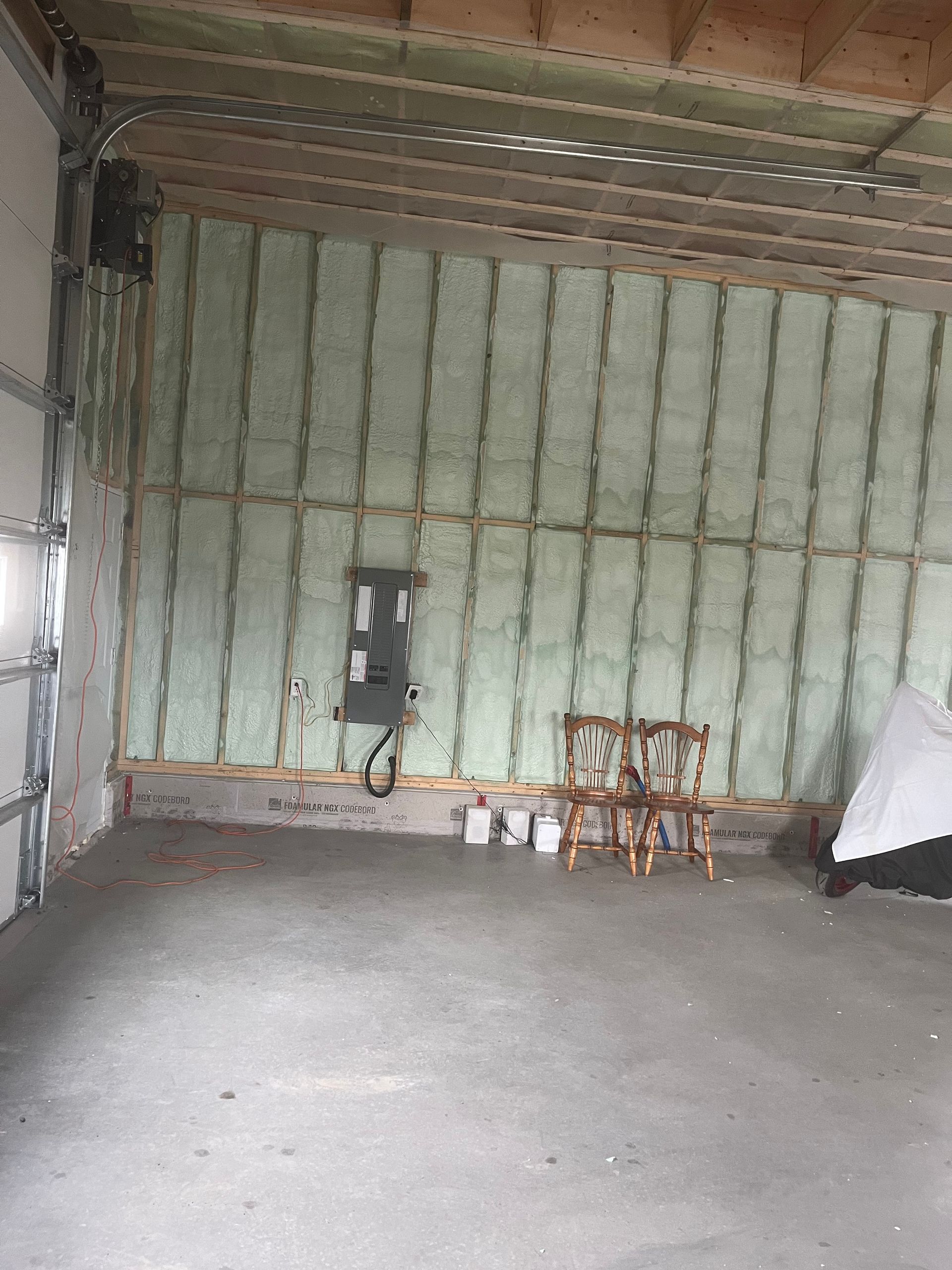 Empty unfinished room with insulated walls, concrete floor, and a small workbench with supplies.