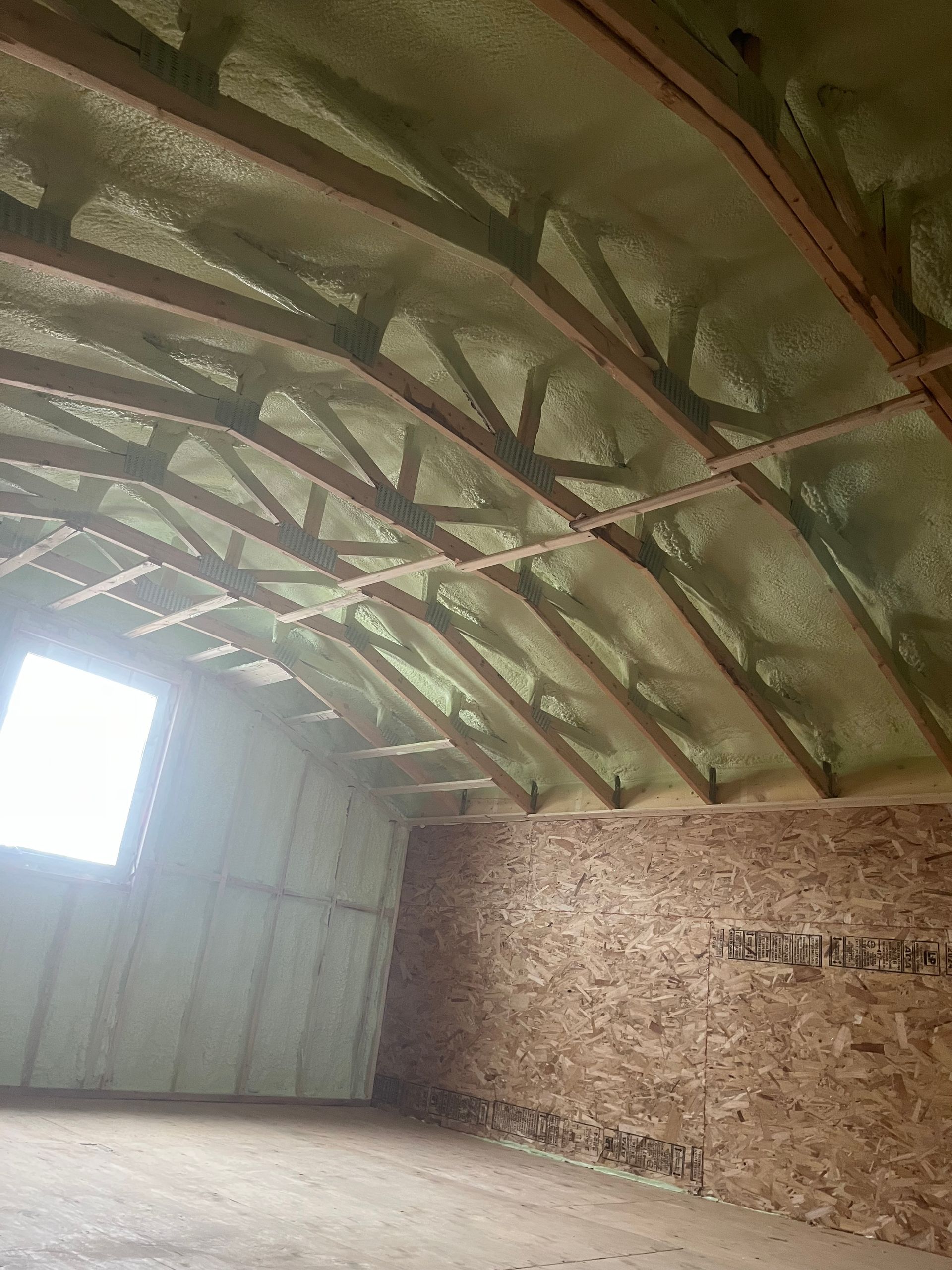 Empty barn interior with a curved metal roof and plywood walls, lit by a bright window.