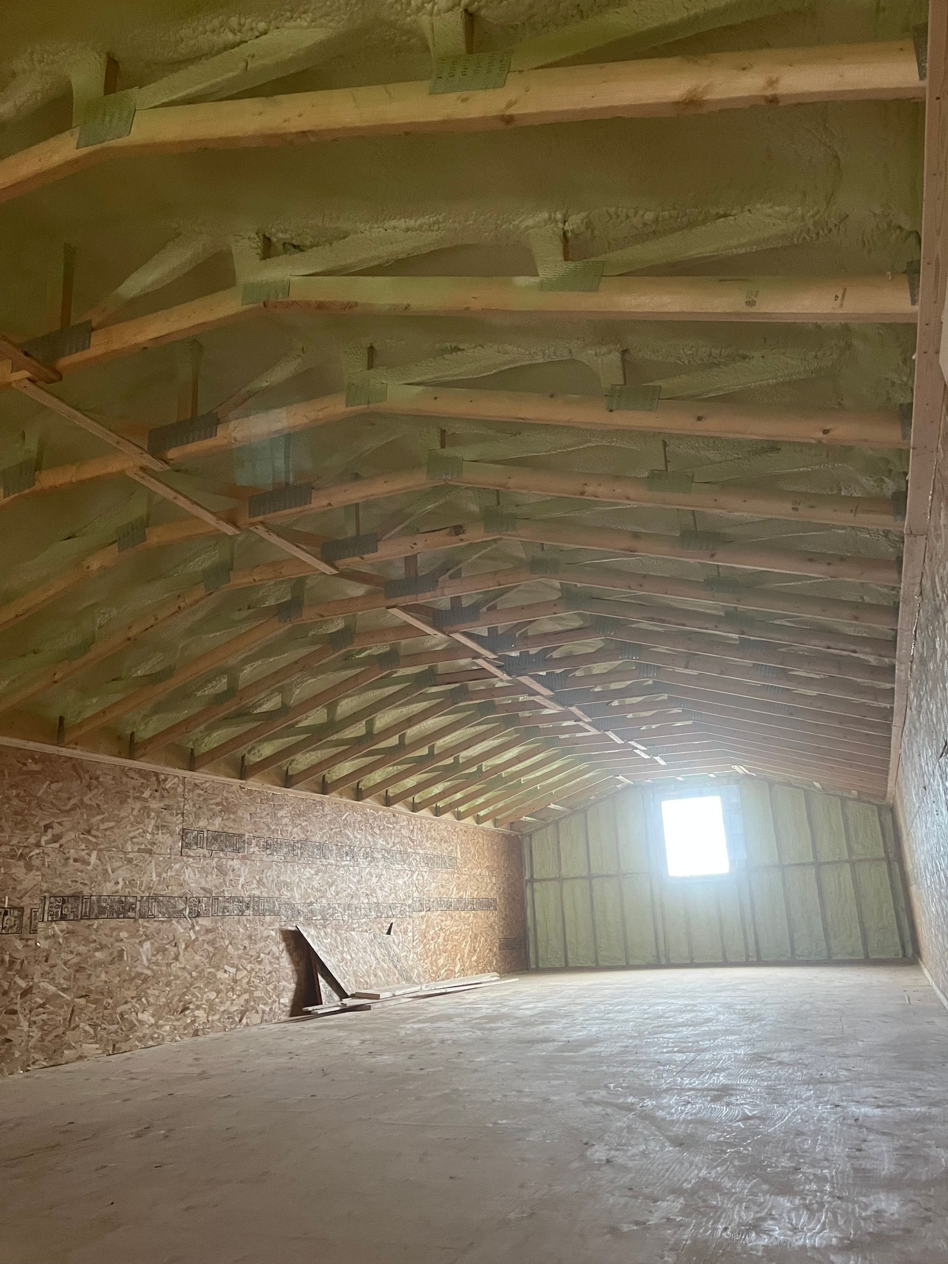 Empty wooden barn interior with slanted rafters, hay-covered walls, and a bright window at the far end