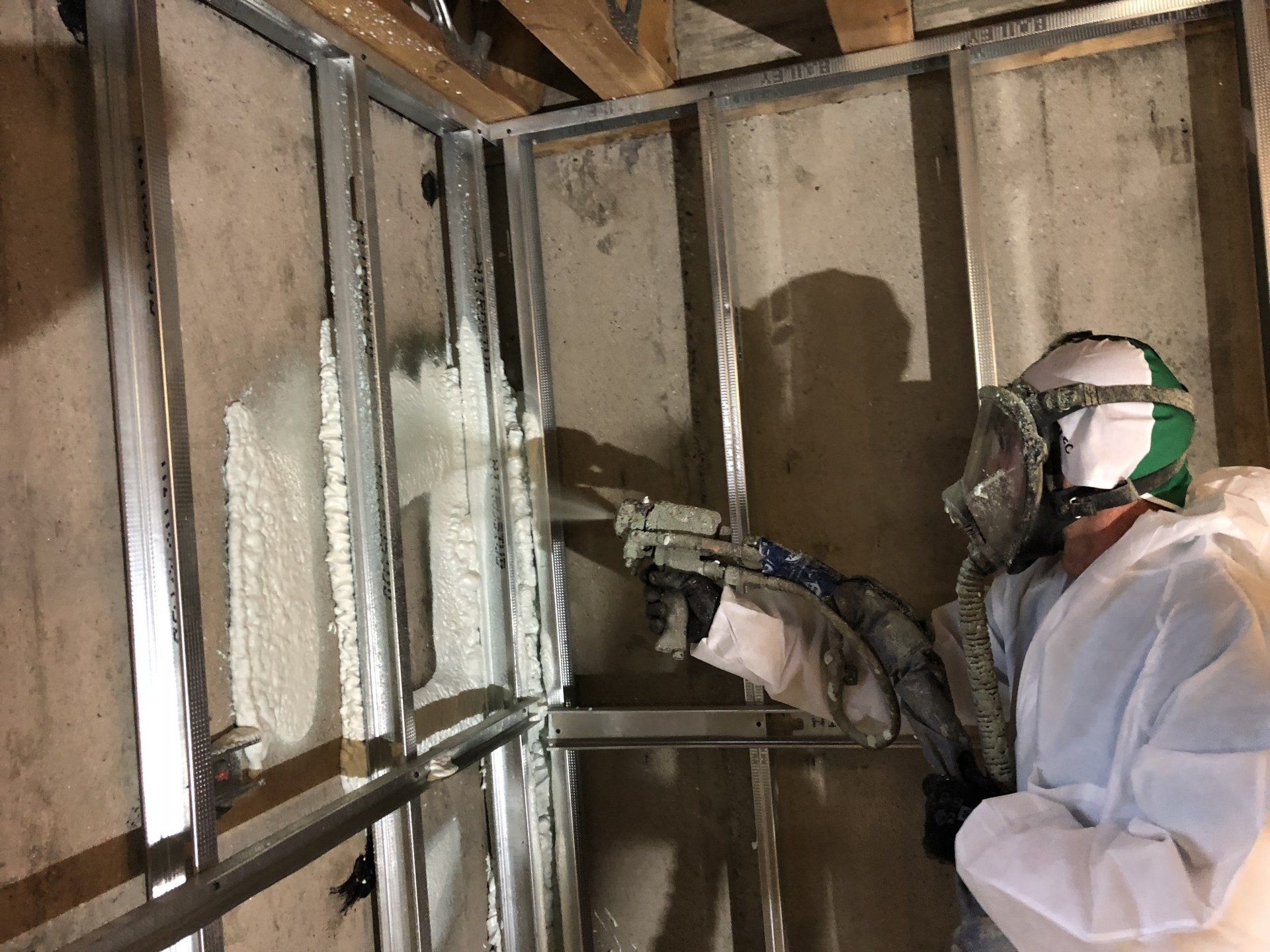 Worker spraying insulation foam inside exposed wall studs during construction