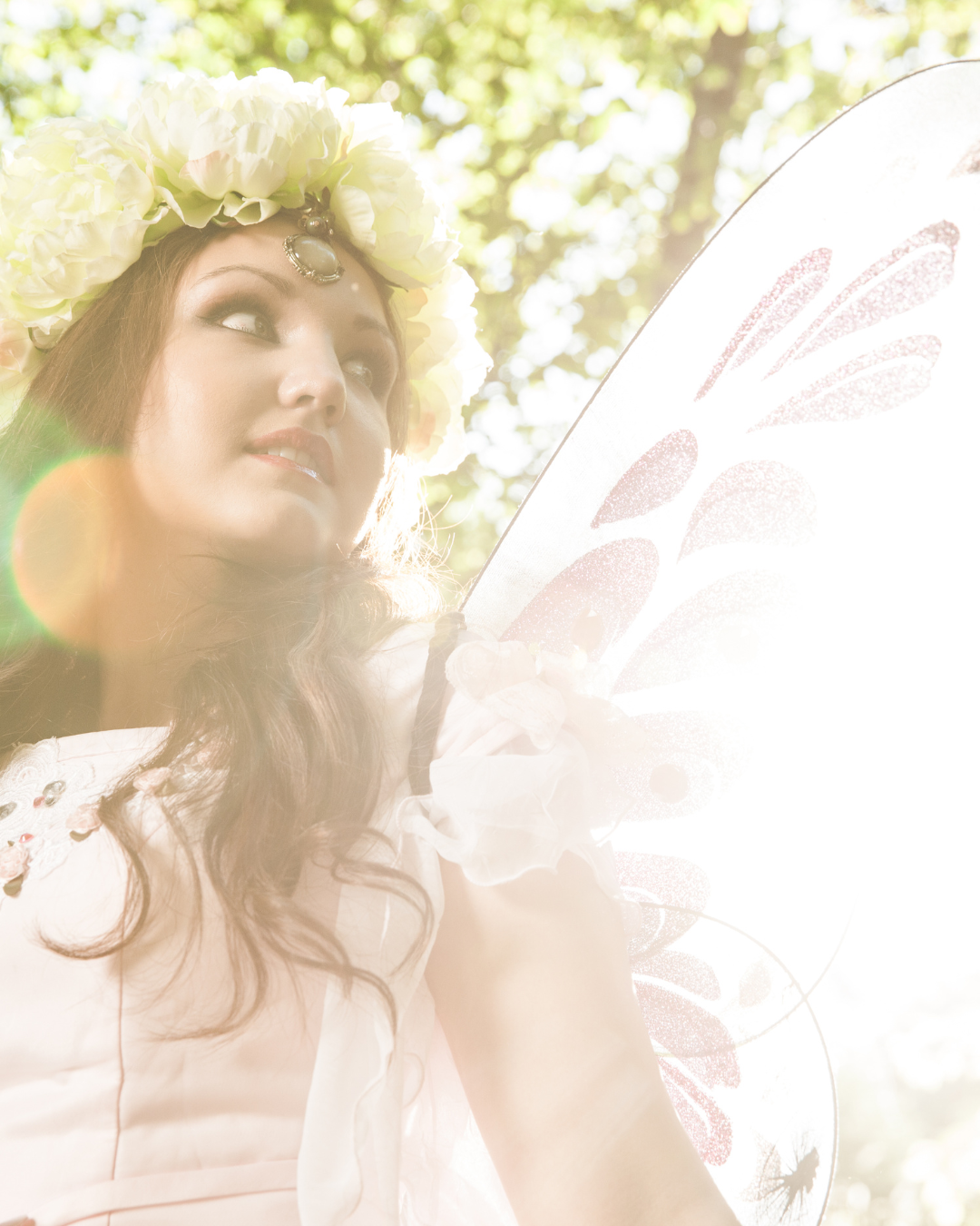 A woman wearing a flower crown and wings is holding a fan.