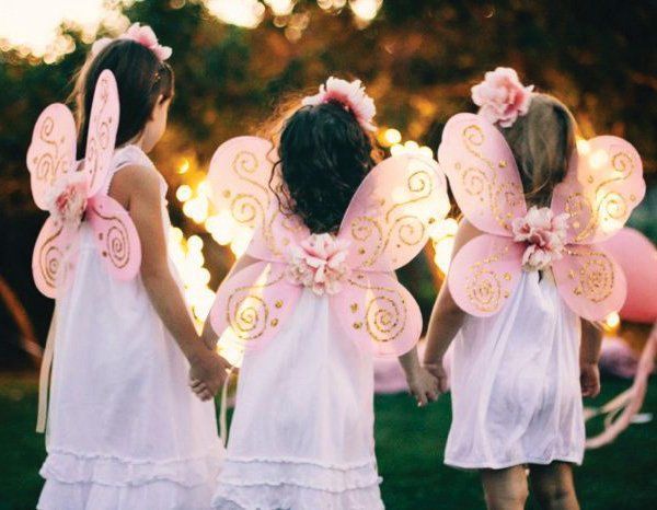 Three little girls wearing pink fairy wings are holding hands