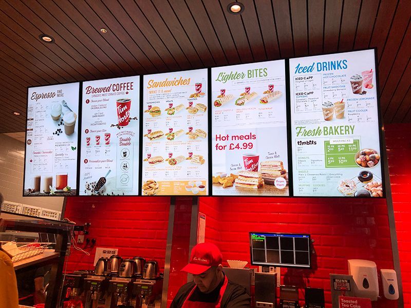 Digital menu boards above a red counter, displaying food and drink options.
