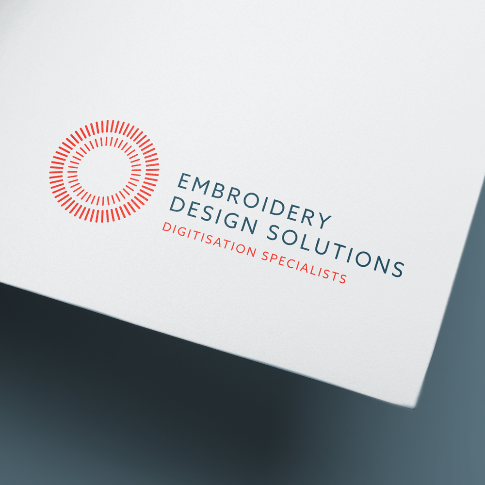 Logo for Embroidery Design Solutions with a red circular icon and blue and red text on a white background.