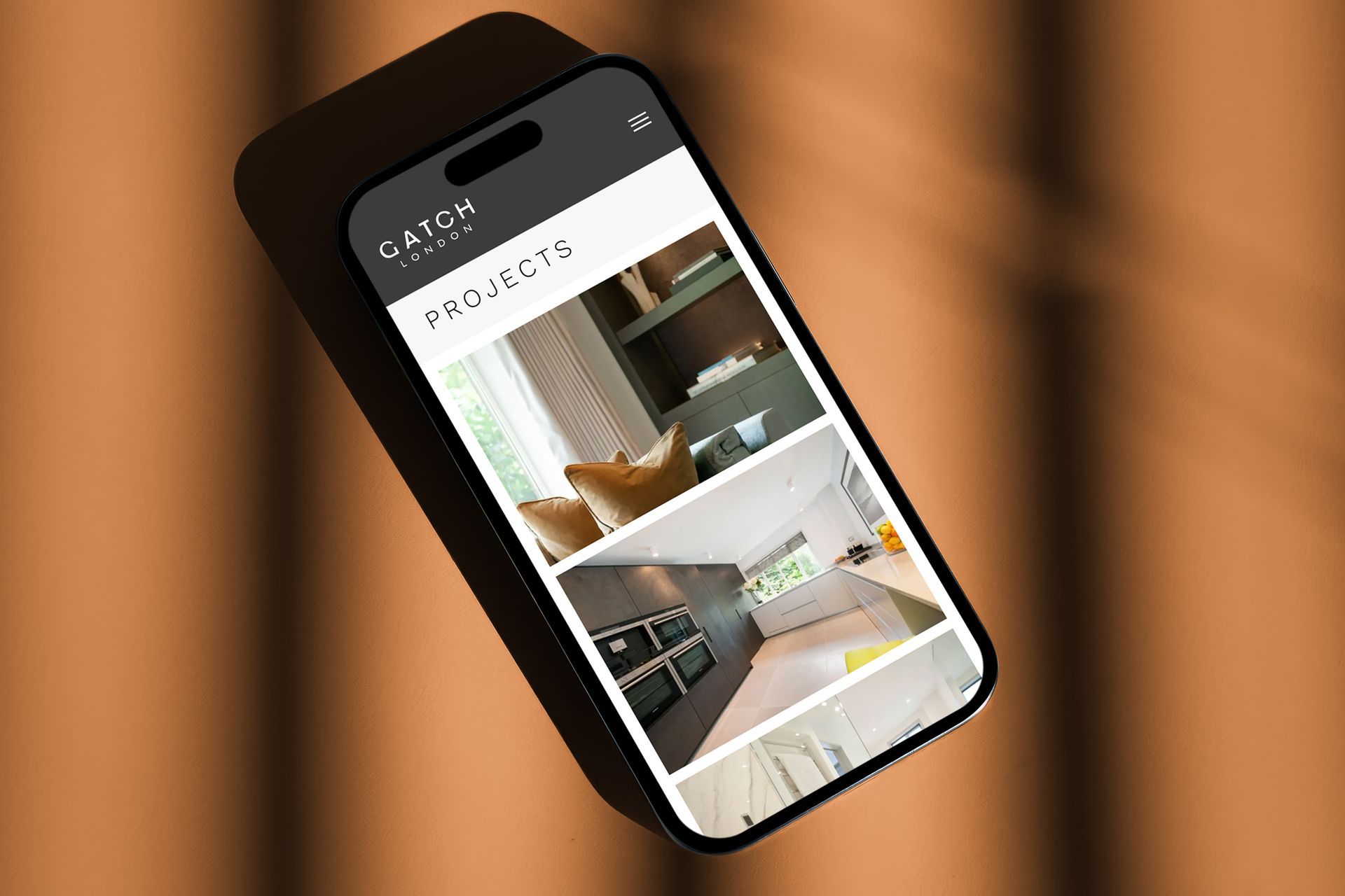 Smartphone displaying a website with interior design photos on a brown background with shadows.