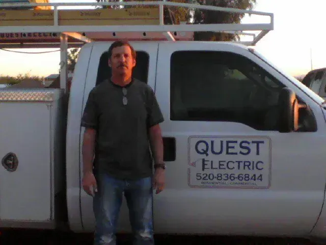 Man standing beside a white QUEST Electric service truck with ladder racks at sunset Man standing beside a white QUEST Electric service truck with ladder racks at sunset