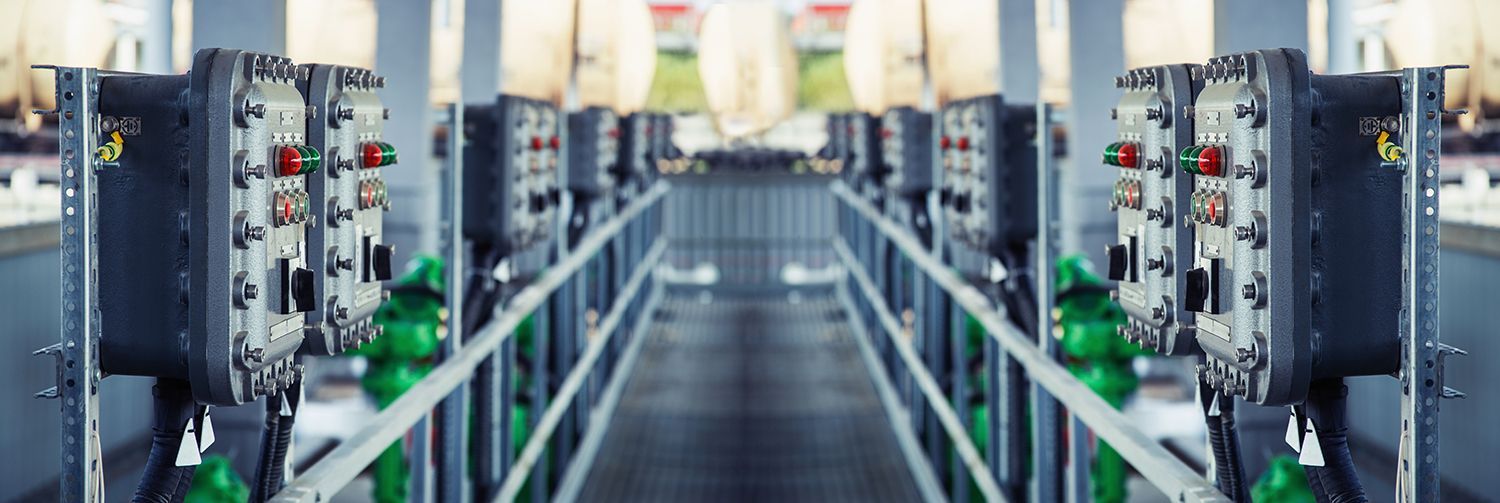 Rows of industrial machines in a factory aisle with green conveyor rails and overhead lights