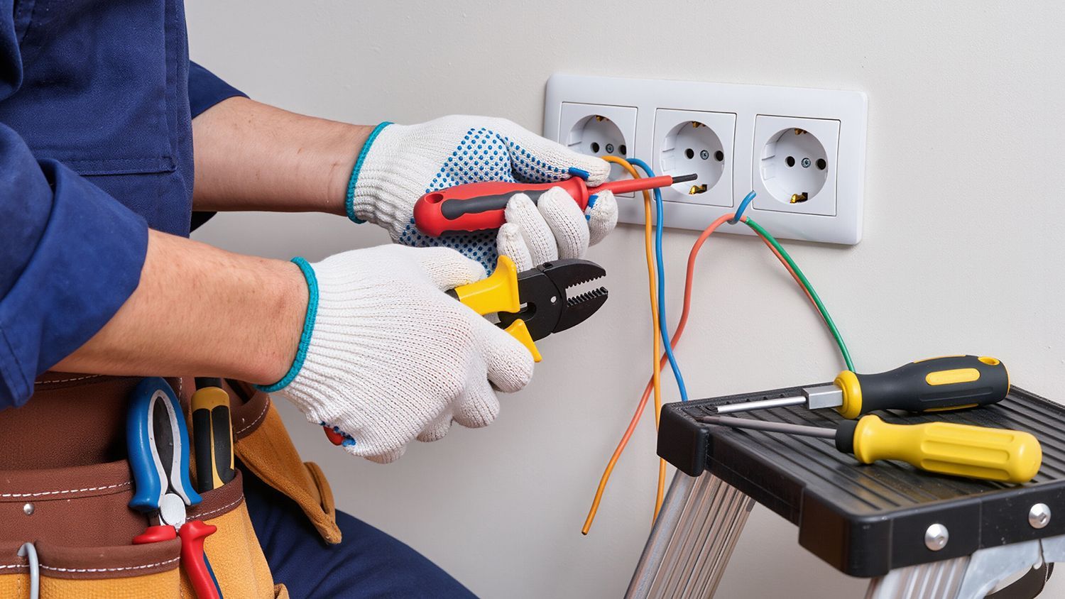 Electrician testing wiring at a wall outlet with insulated tools and exposed wires Electrician testing wiring at a wall outlet with insulated tools and exposed wires