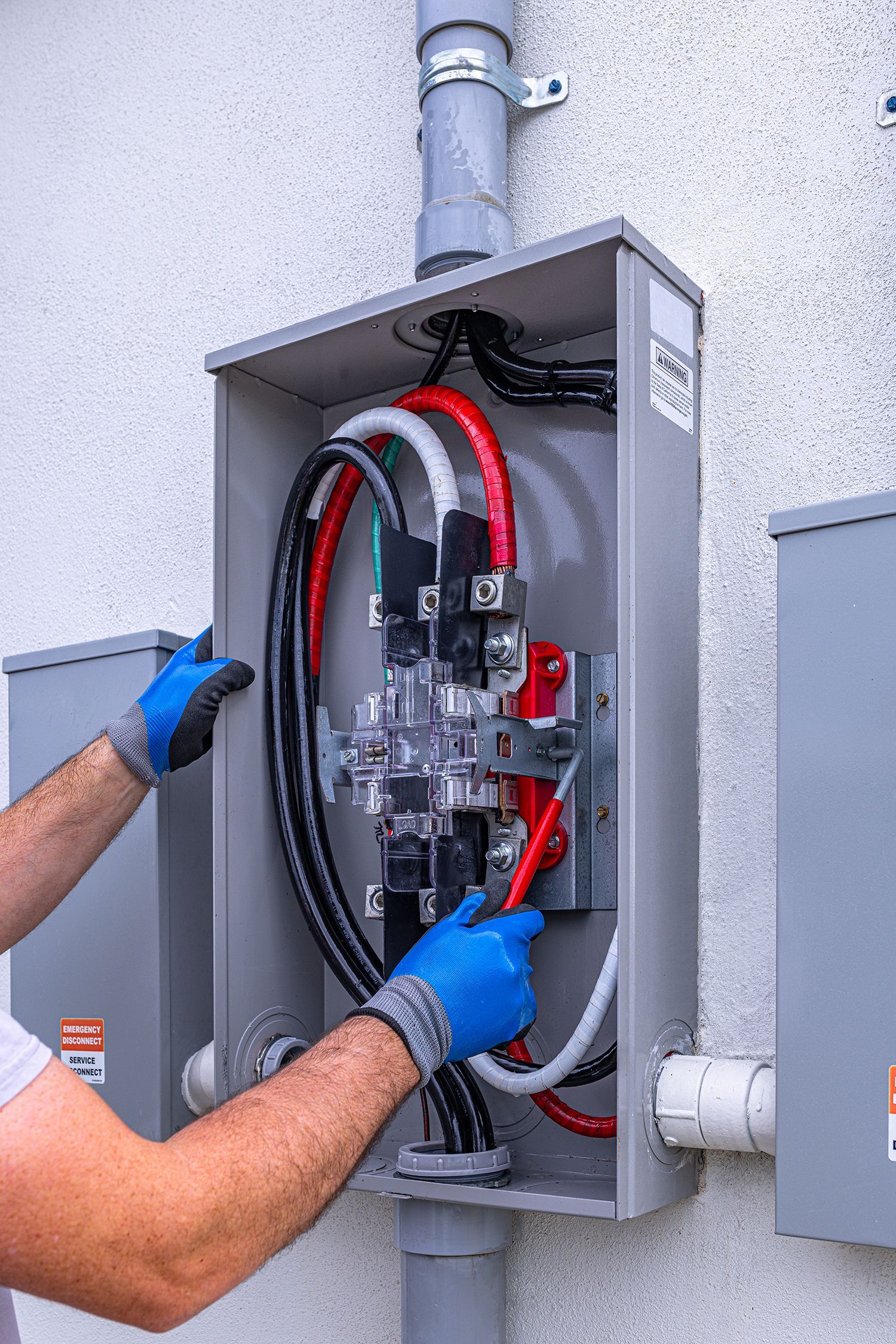 Person working inside an open electrical panel with red and black cables, wearing blue gloves.